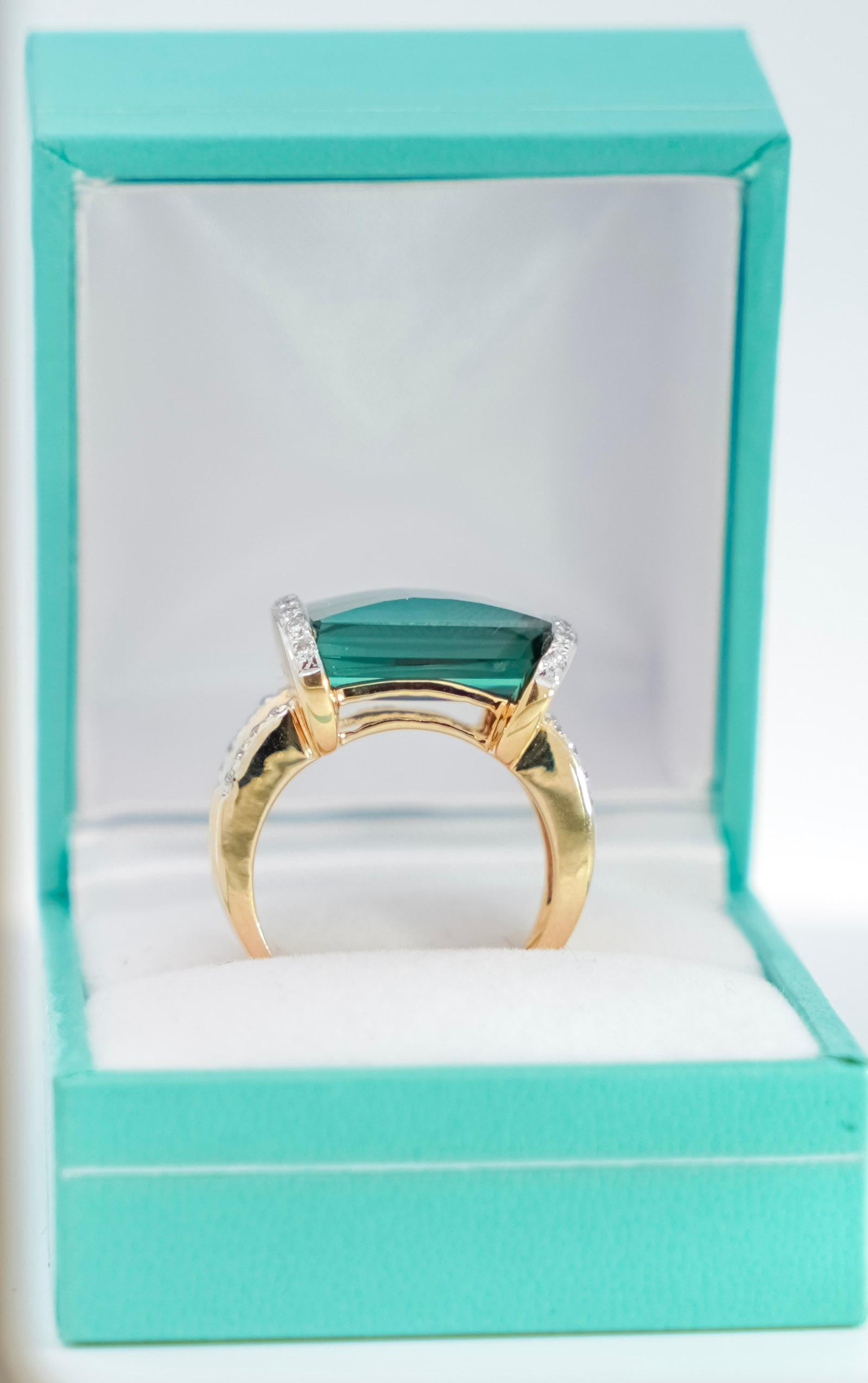 GIA Certified 18k two tone solid gold mounts an octagonal step-cut Tourmaline with round-cut diamond side stones. Centering a Blue-Green Tourmaline with charming facets that dazzle as the ring moves. Half bezel set, with a masterfully carved gold