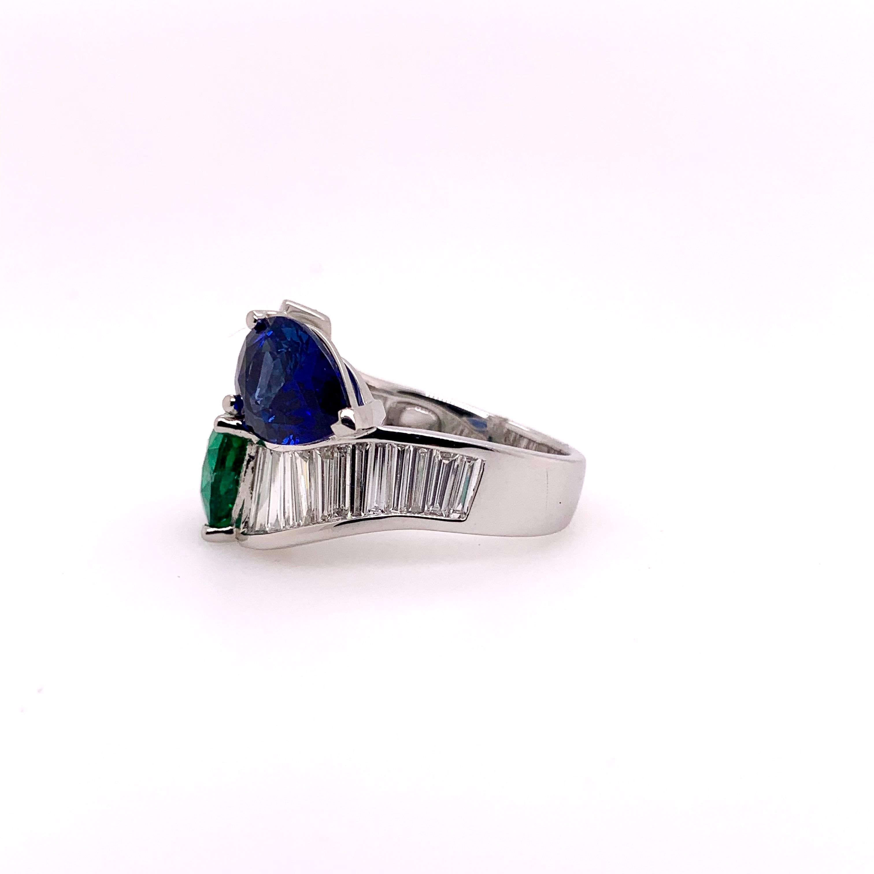 Stunning blue sapphire and emerald bypass ring accompanied by extra long tapered baguettes!  The heated 4.15 ct blue sapphire is GIA certified and is opposed by a 3.99 ct Zambian emerald in a platinum setting.  The 2.00 cts of extra long baguettes