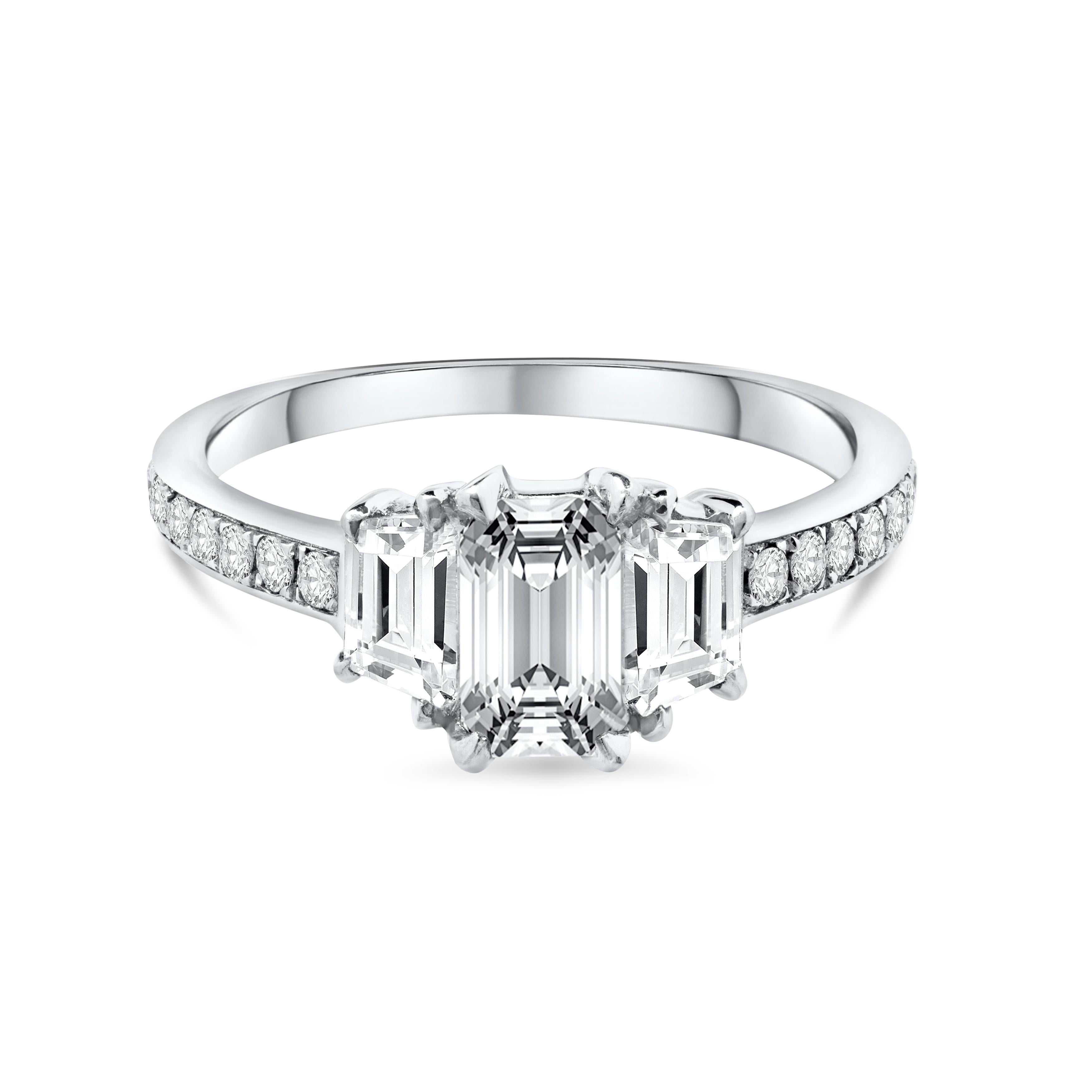 Classic and elegant in style, this three stone ring is set with a gorgeous 0.70 carat emerald cut diamond center certified by GIA as F color and SI1 clarity. Flanked by a trapezoid diamond on either side, weighing 0.45 carat total. Accented with