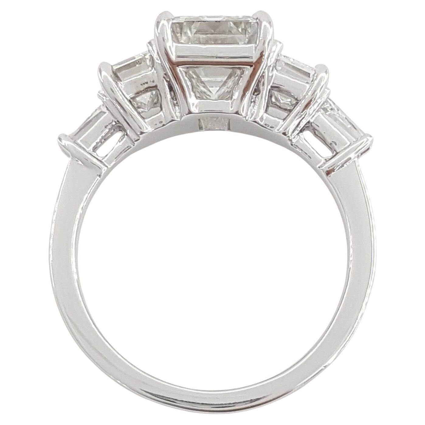 This platinum engagement ring features a total weight of 3.8 carats, comprising emerald and baguette cut diamonds. The ring itself weighs 7.2 grams and is size 6.5. Its centerpiece is a natural ideal emerald cut diamond, weighing 2.56 carats, with E