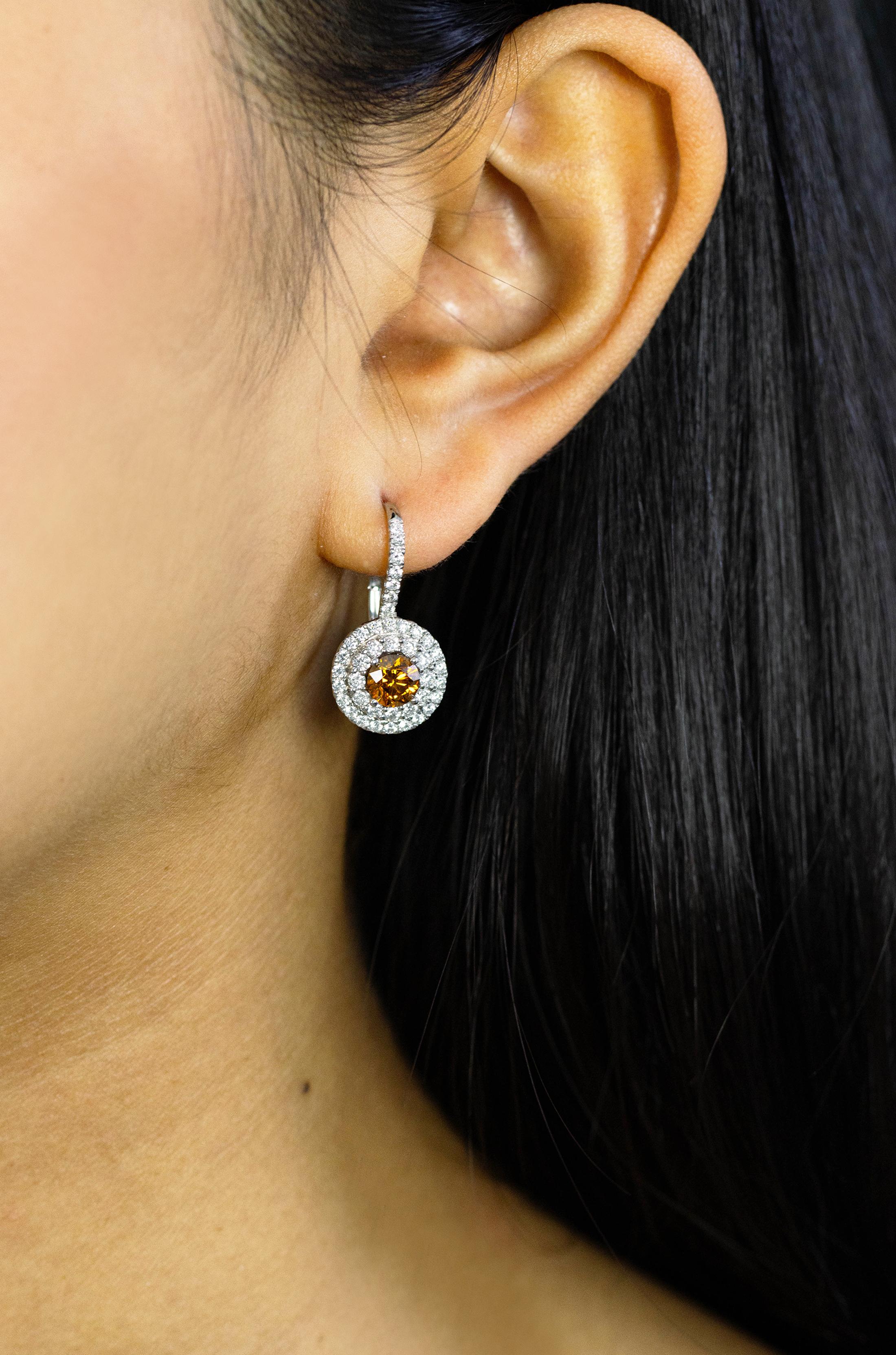 This beautiful pair of earrings feature 2 GIA Certified center stones weighing 0.65 and 0.67 carats respectively. GIA certified the stones as having a Fancy Deep Yellow Orange color. Both stones are accented by 2 rows of round brilliant diamonds