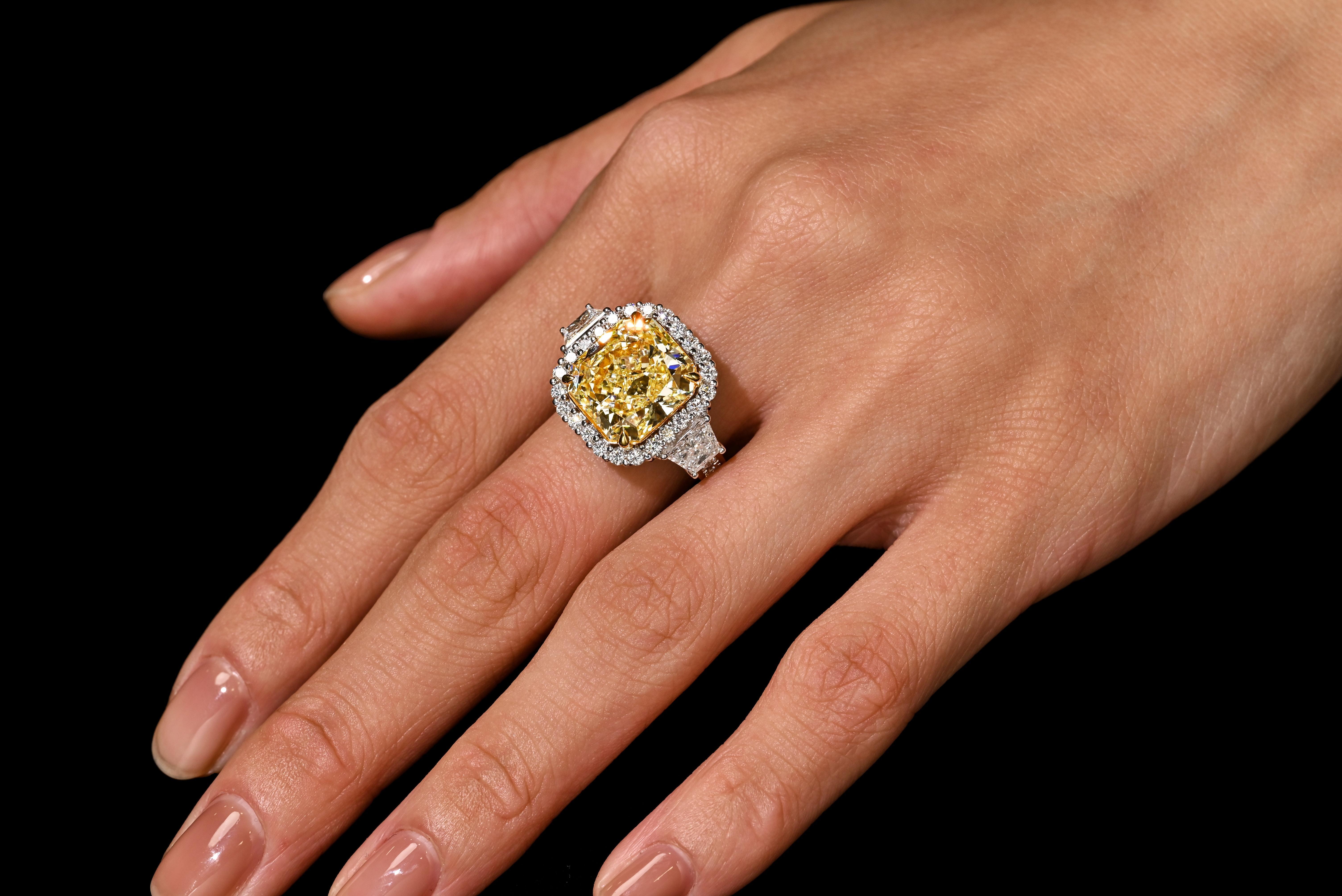 Substantial and breathtaking GIA certified 8.39 carat radiant cut fancy intense yellow diamond ring. Featuring 2 trapezoid cut diamond side stones and a round cut diamond halo and ring shank. Set in 18k white gold with yellow gold prongs. The ring
