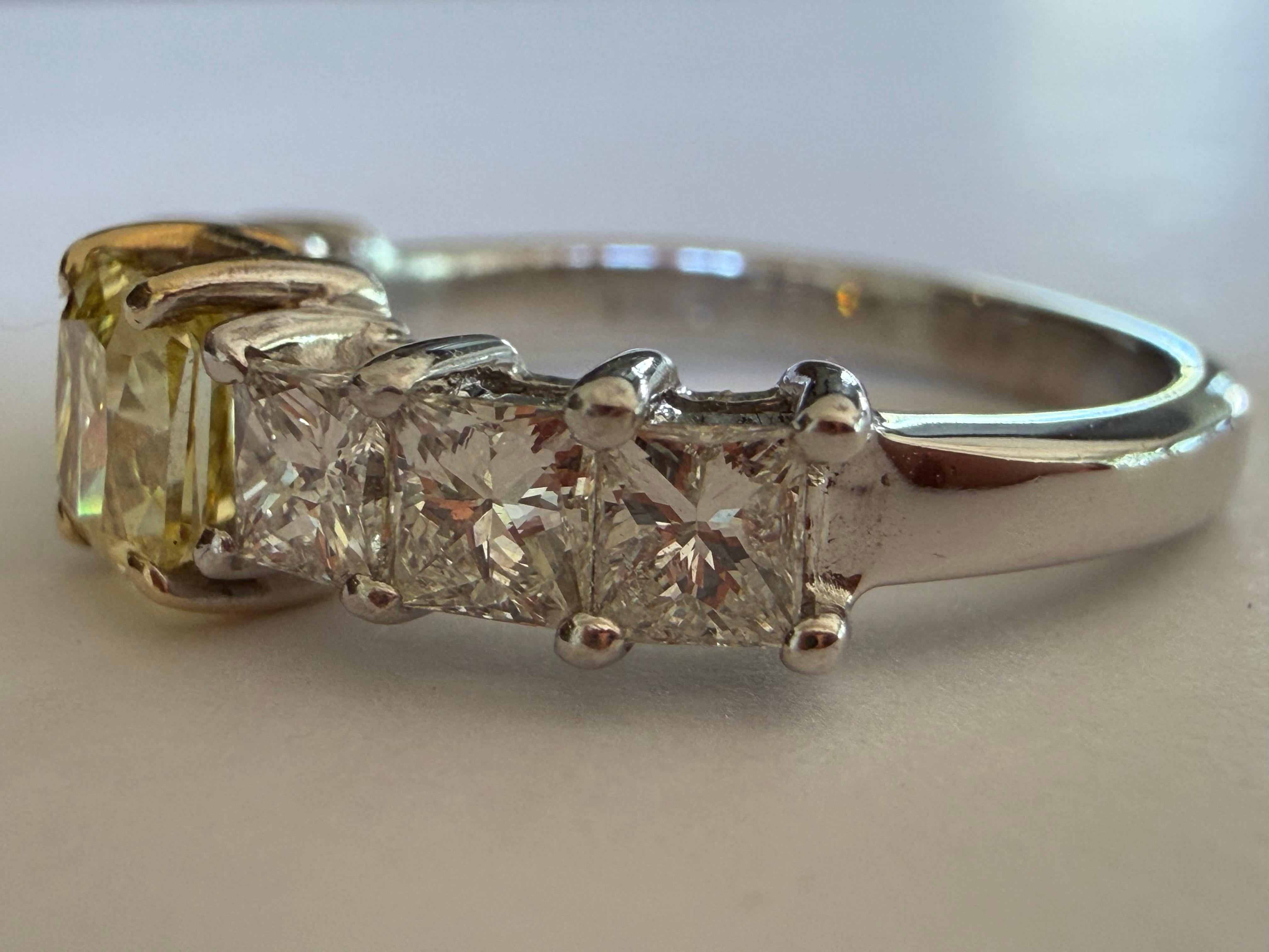 Cette bague exquise est ornée d'une pierre centrale en diamant de taille radiant de couleur jaune fantaisie naturelle, pesant 0,55 carat. Cette pièce maîtresse remarquable est joliment flanquée de chaque côté de trois diamants blancs de taille