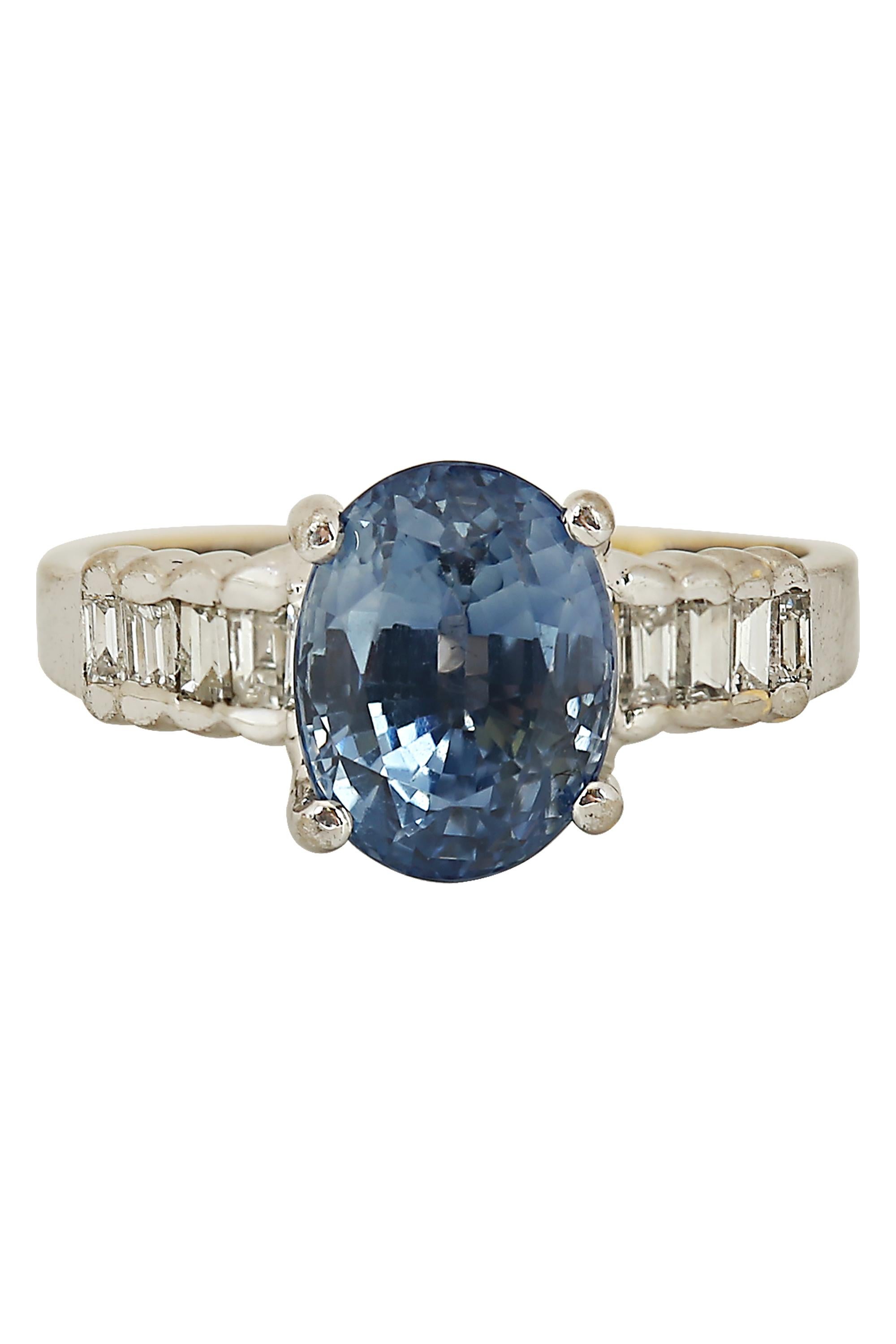 This ring features a delicately hued lavender fancy cut oval sapphire accentuated by shoulders of baguette cut diamonds in a 14 karat white gold mounting. The lavender sapphire weighs approximately 4 carats and is certified by GIA. Currently a size