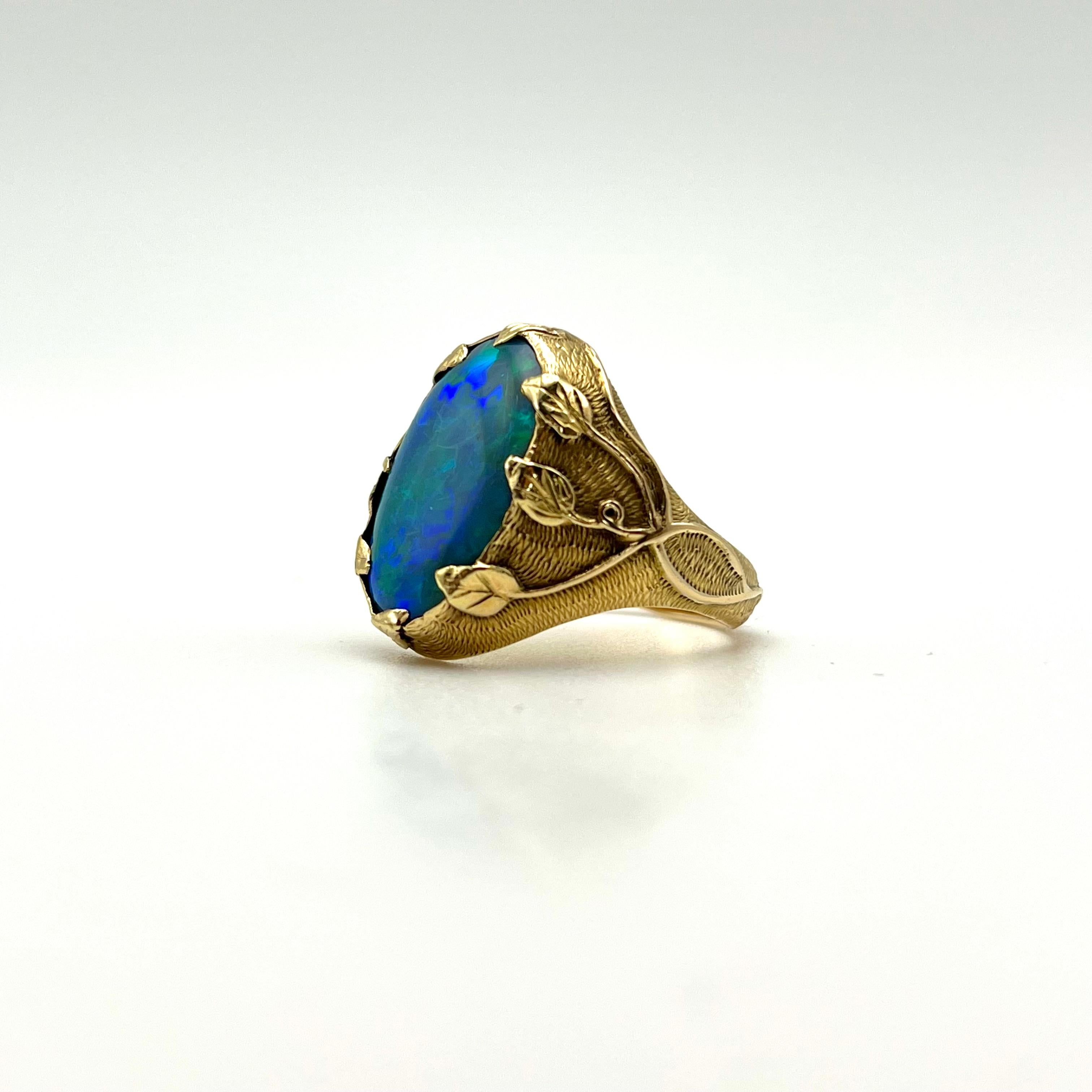 This stunning, GIA-certified natural opal is set in a 14-karat gold Art Nouveau mounting. This foliage-inspired piece features intricate vine designs along the shank. This craftsmanship extends to the prongs, securing the opal in place with small,