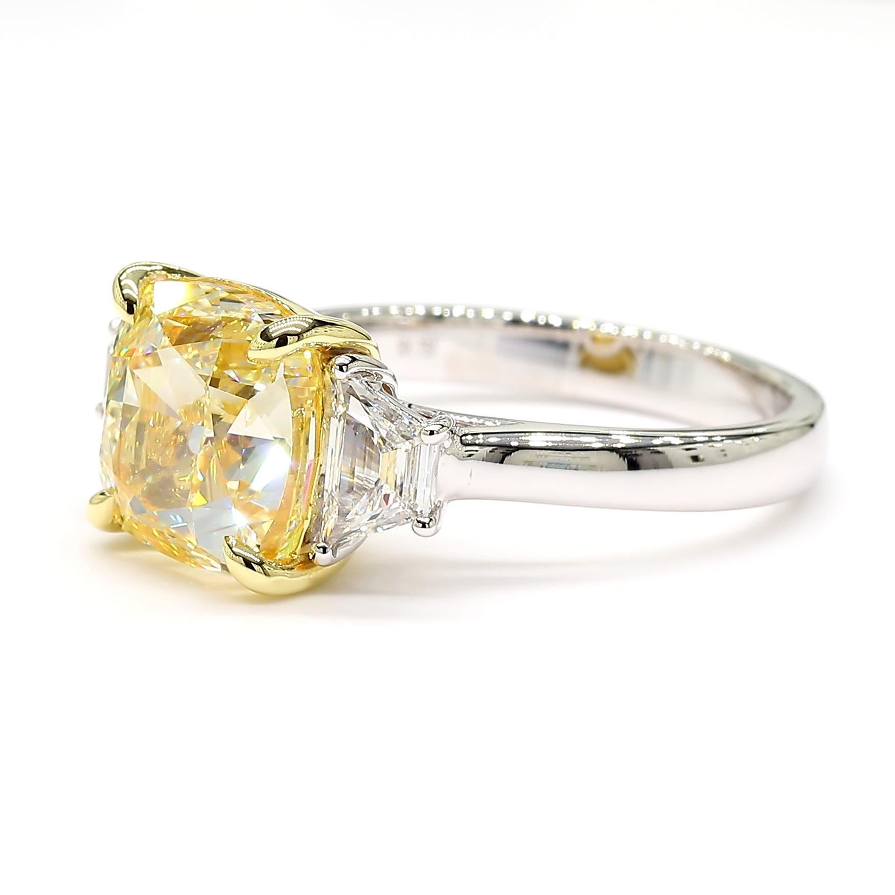 La magnifique bague en diamant certifiée GIA de Raregemworld. Monté dans une belle monture en or jaune et blanc 18 carats avec un diamant jaune naturel de taille coussin. Le diamant jaune est entouré de diamants blancs de taille trapézoïdale