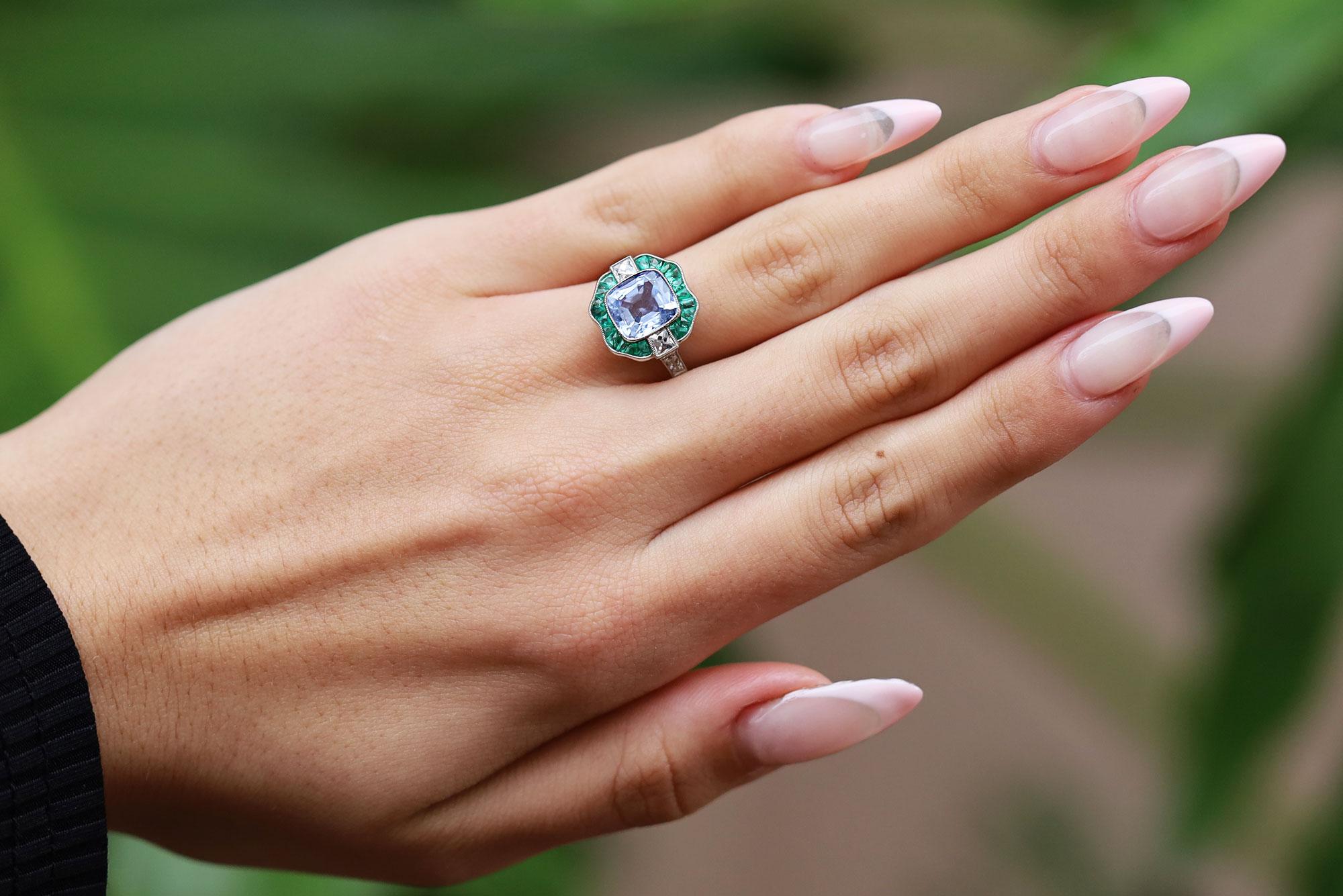 An incredible and rare unheated Ceylon sapphire is the center of attention of this gorgeous multi-gemstone ring. The Calibré emeralds hug the border of the spectacular cornflower blue sapphire and delivers a truly appealing color combination. Old