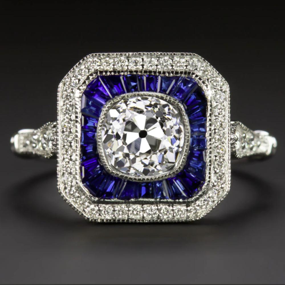 This exceptional Art Deco-style ring features a vibrant 0.77 carat GIA certified Old European cut diamond, framed by a bold double halo of calibre cut sapphires and round white diamonds. The center stone boasts a romantic vintage character, with
