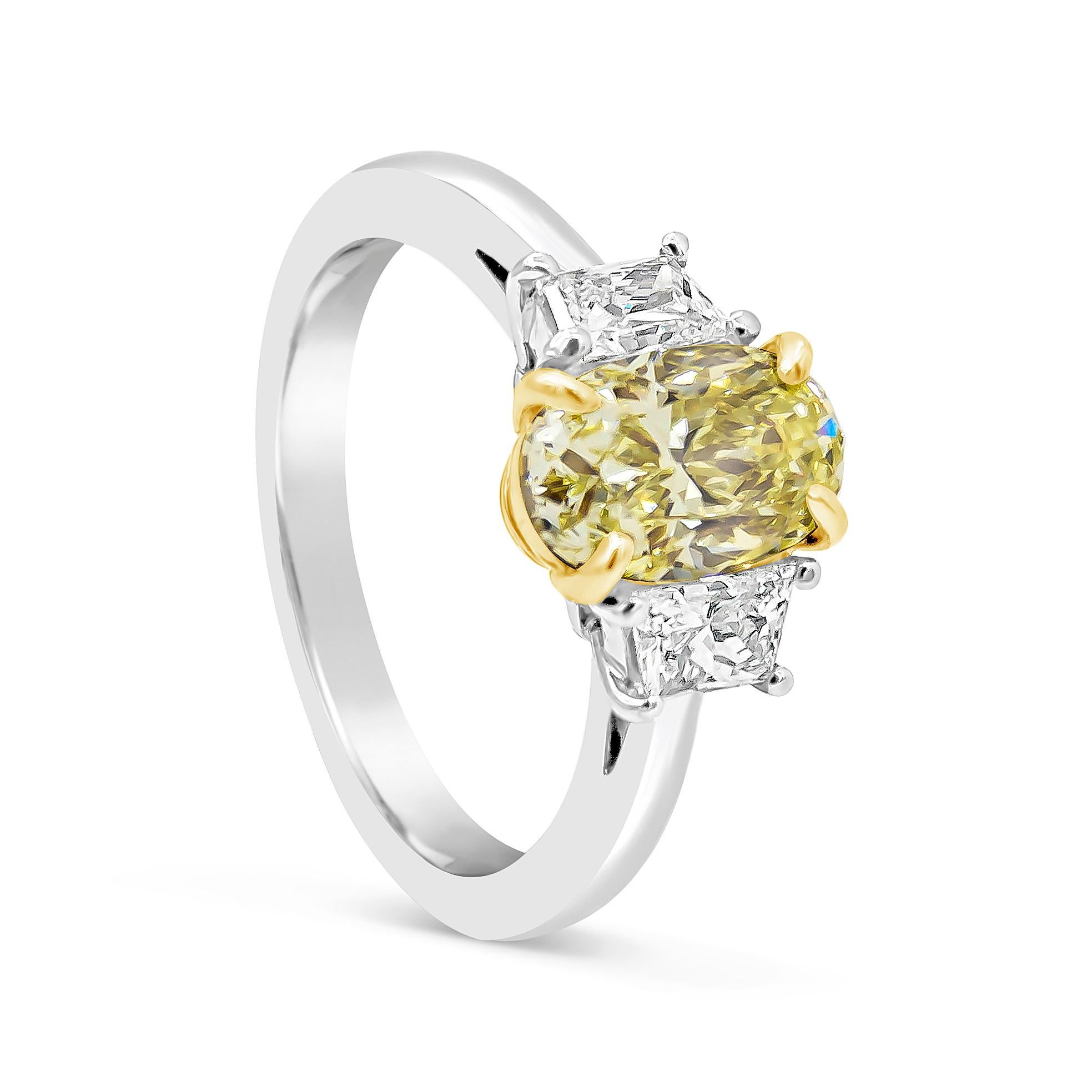 Showcasing a color-rich 1.57 carats oval cut yellow diamond certified by GIA as Fancy Yellow color and VS1 clarity, set in a four prong 18K yellow gold. Flanked by two trapezoid diamonds weighing 0.50 carats total, set in a polished platinum