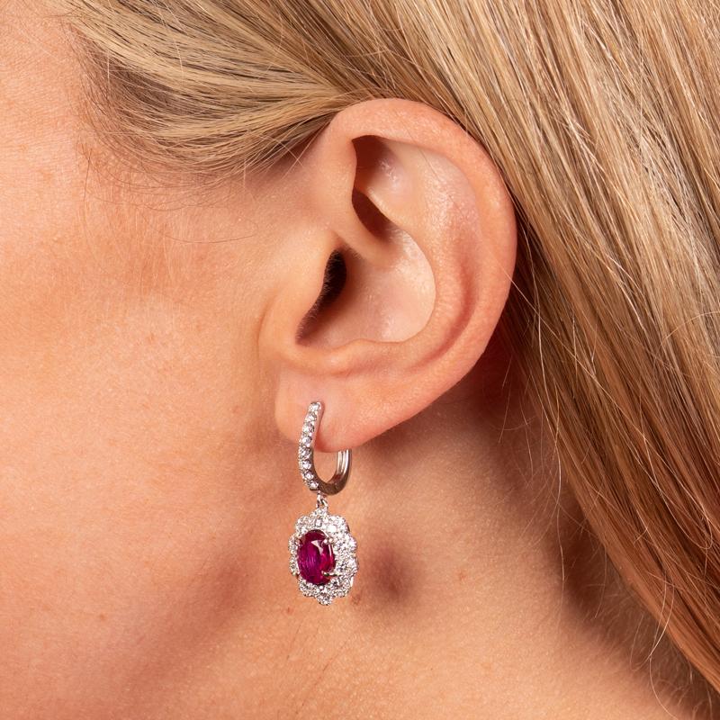 These beautiful dangle earrings feature two GIA certified oval shaped rubies measuring 2.42 carats and 1.81 carats. They are accented by 1.37 carat total weight in round brilliant diamonds. These earrings are set in 18 karat white gold and dangle