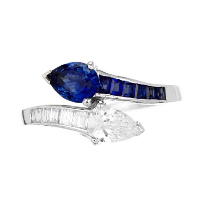 Unique diamond and sapphire platinum bypass cocktail ring. Pear shaped diamond with swirl of graduated baguette diamonds half way down the shank with a matching pear shaped natural deep blue sapphire on the opposite side followed by graduated square