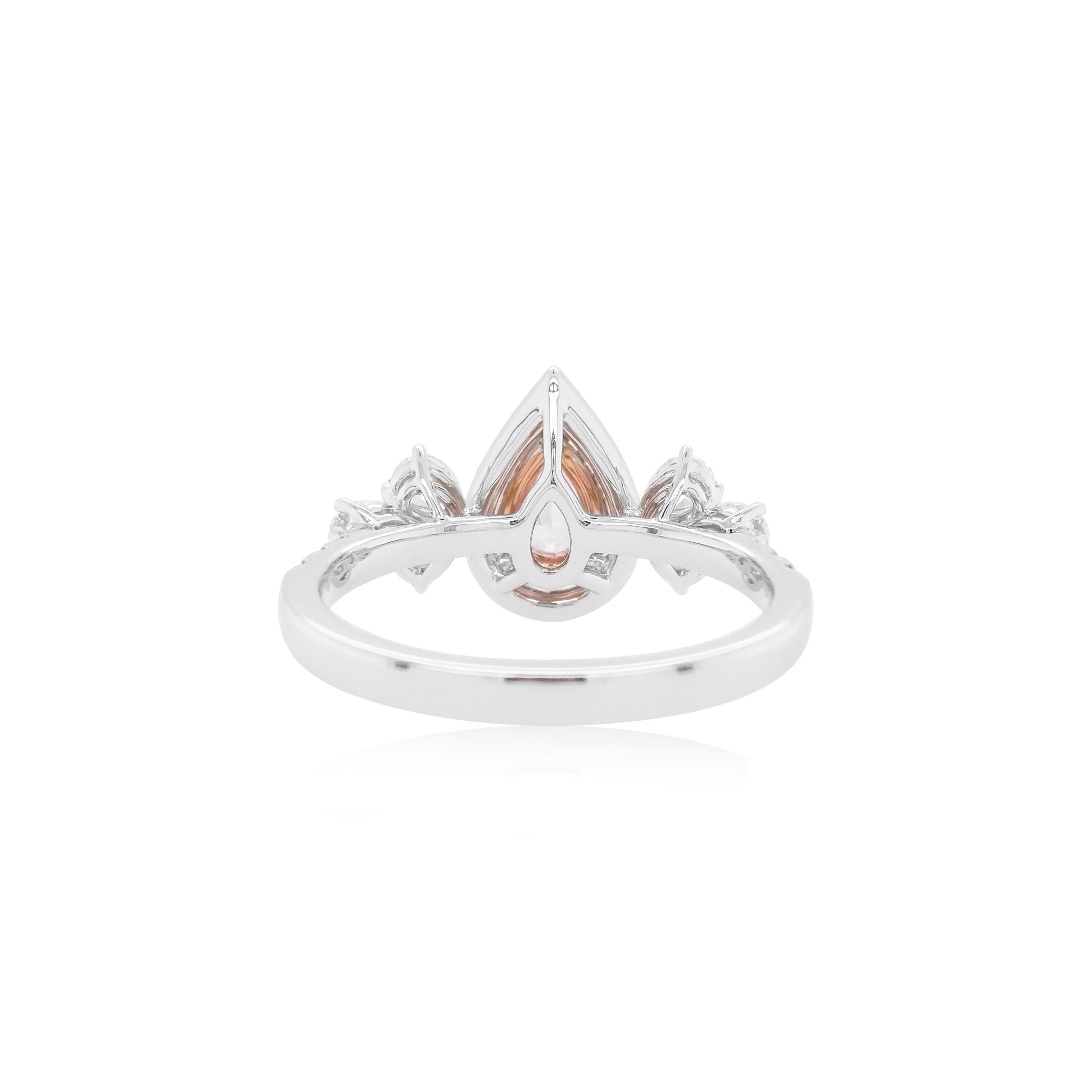 This exquisite ring showcases a stunning pear-shaped GIA Certified  Fancy Pink diamond and a halo of Pink and white diamonds, elegantly flanked by pear-shaped white diamonds. The designer setting enhances its beauty, making it a truly remarkable
