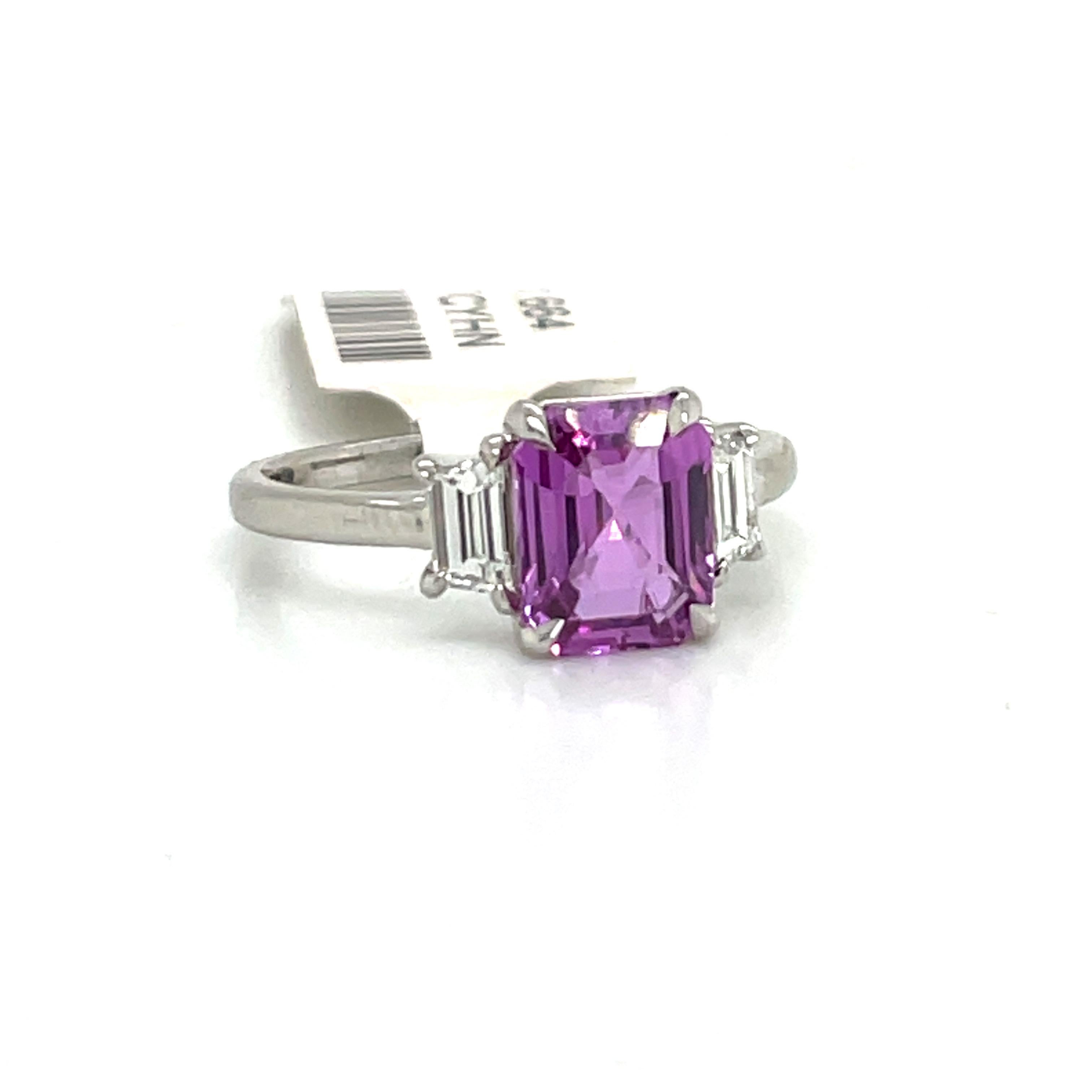 Platinum three stone ring featuring one GIA Certified Emerald Cut Pink-Purple Sapphire No Heat flanked with two Trap diamonds weighing 0.45 Carats. Color H 
Clarity VS1