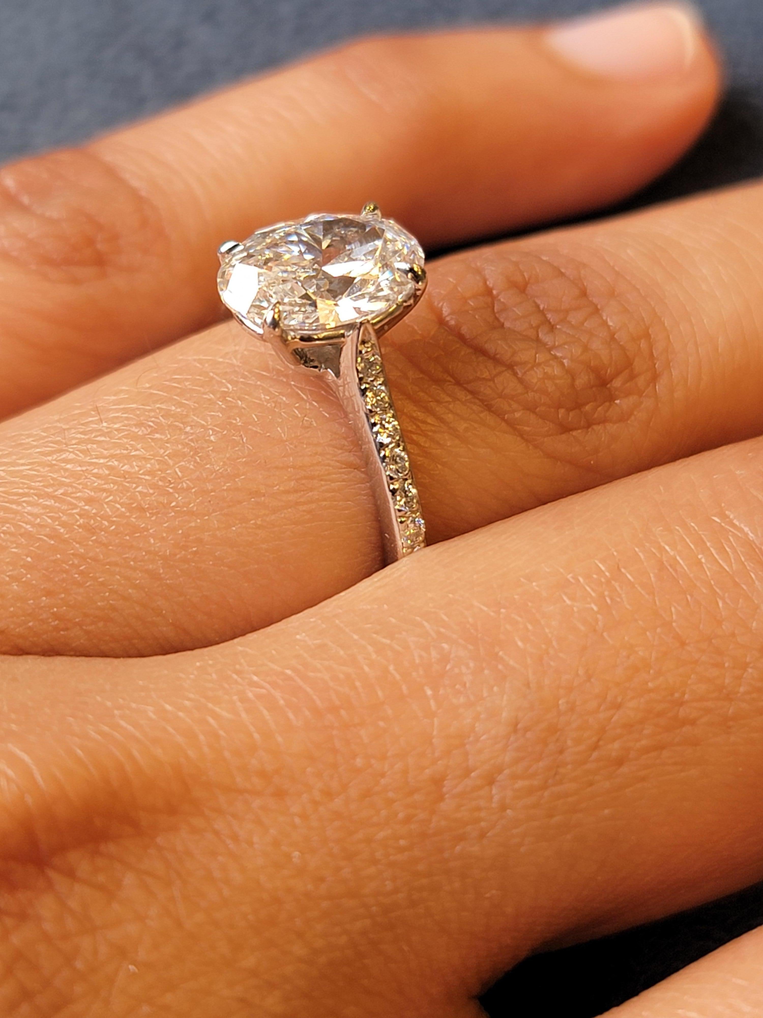 The ring features a beautifully elegant setting that showcases the central Oval diamond, drawing all eyes to its brilliance. The ring is adorned with an exquisite GIA certified platinum Oval-cut Diamond with side round stones half around engagement