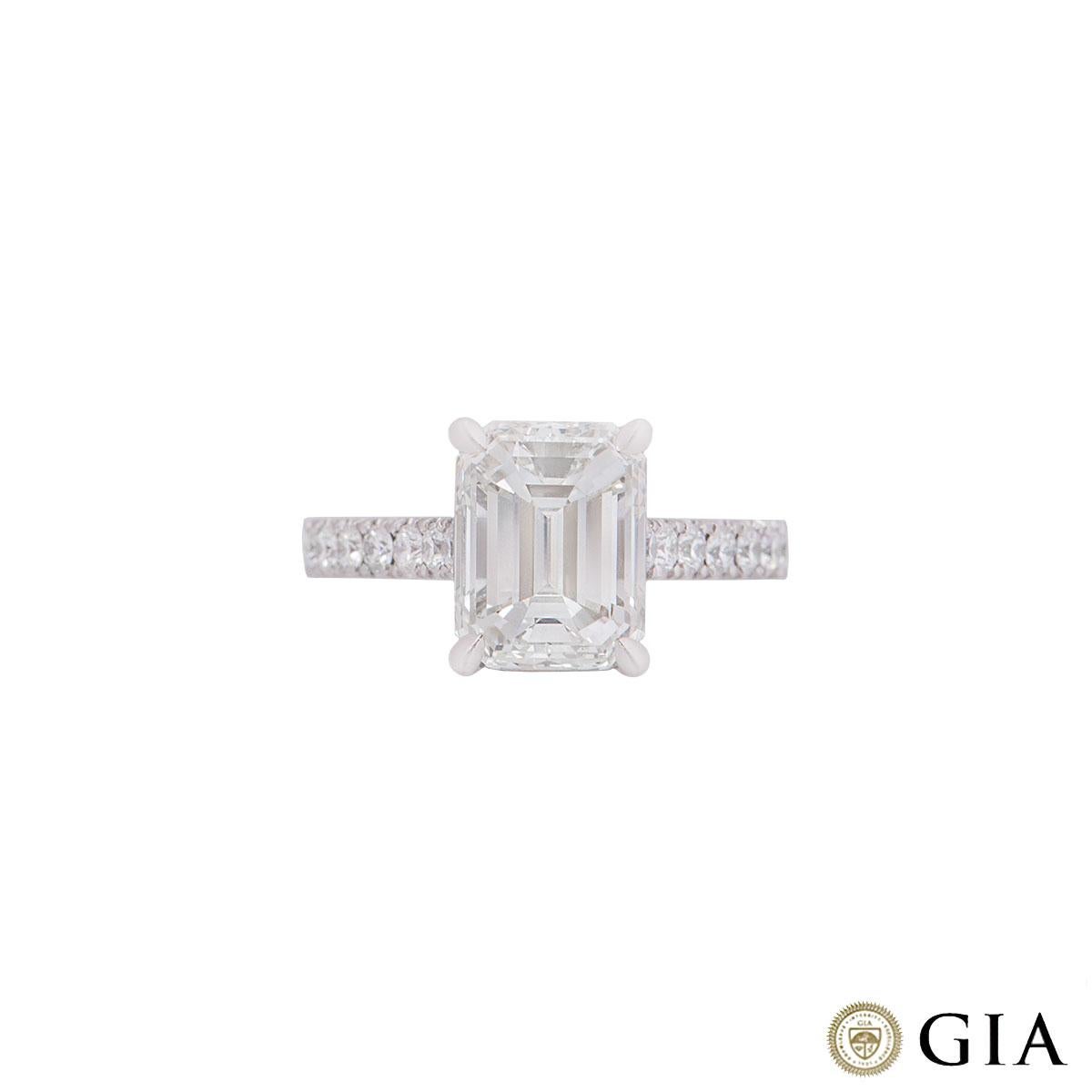 A platinum emerald cut diamond ring. The ring is set to the centre with an emerald cut diamond weighing 3.02ct, I colour and VVS1 in clarity in a four claw setting complemented by round brilliant cut diamonds on the shoulders with an approximate