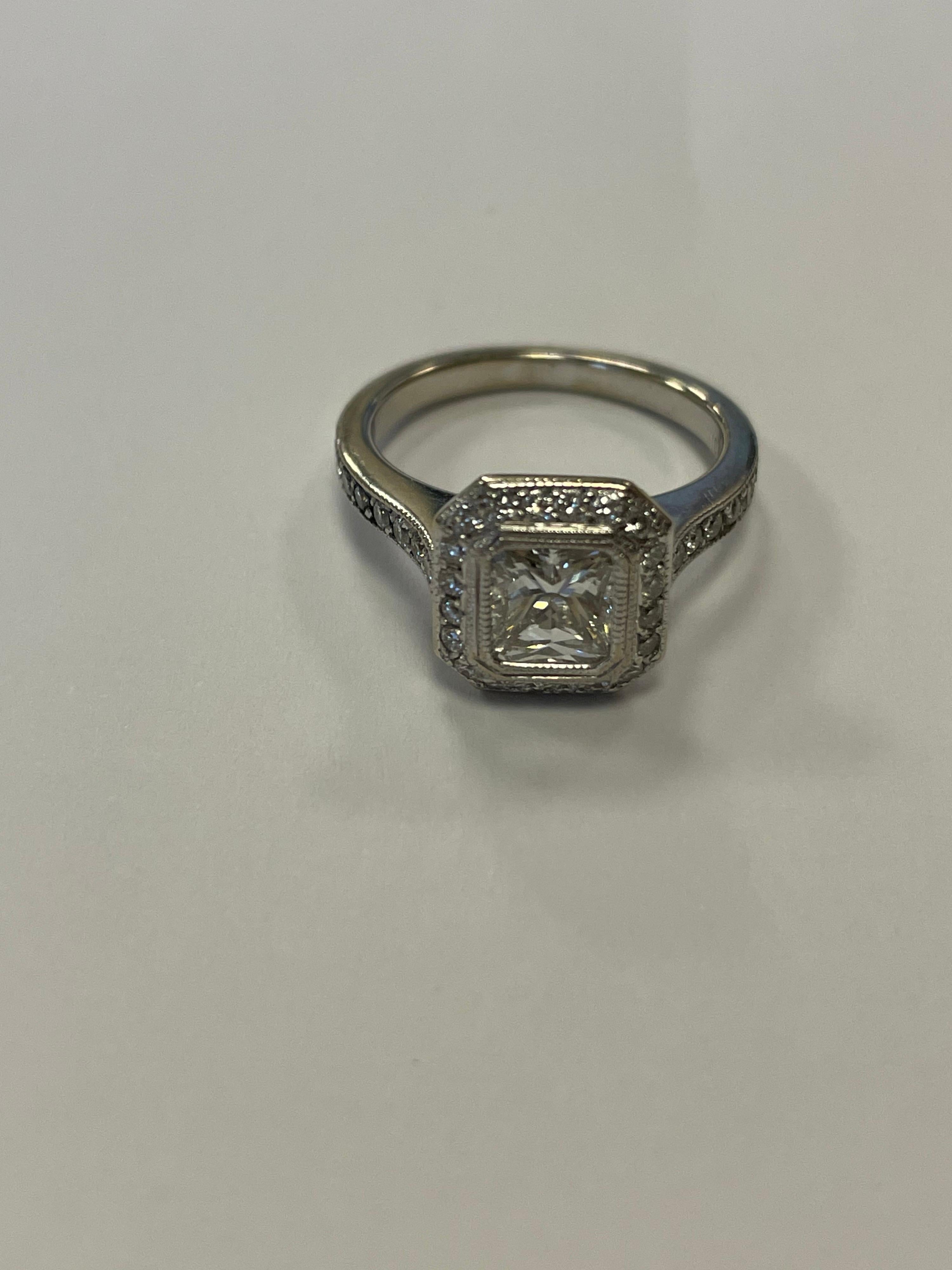 Diamante de talla radiante certificado por el GIA con un peso de 97 qt, color H, claridad SI1, engastado en un halo de oro blanco de 18 quilates con 40 diamantes redondos de talla completa con un peso de 46 qt.
Dedo talla 6, se puede tallar
Última