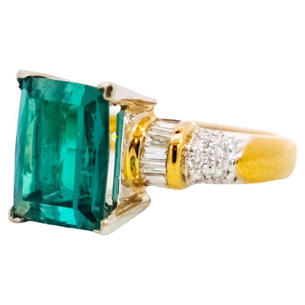 18K yellow gold semi-precious gemstone ring. The center stone is a rectangular-brilliant cut blue-green tourmaline, otherwise known as Indicolite. Complemented by near-colorless round and baguette diamond side stones.

GIA Certification Comment: