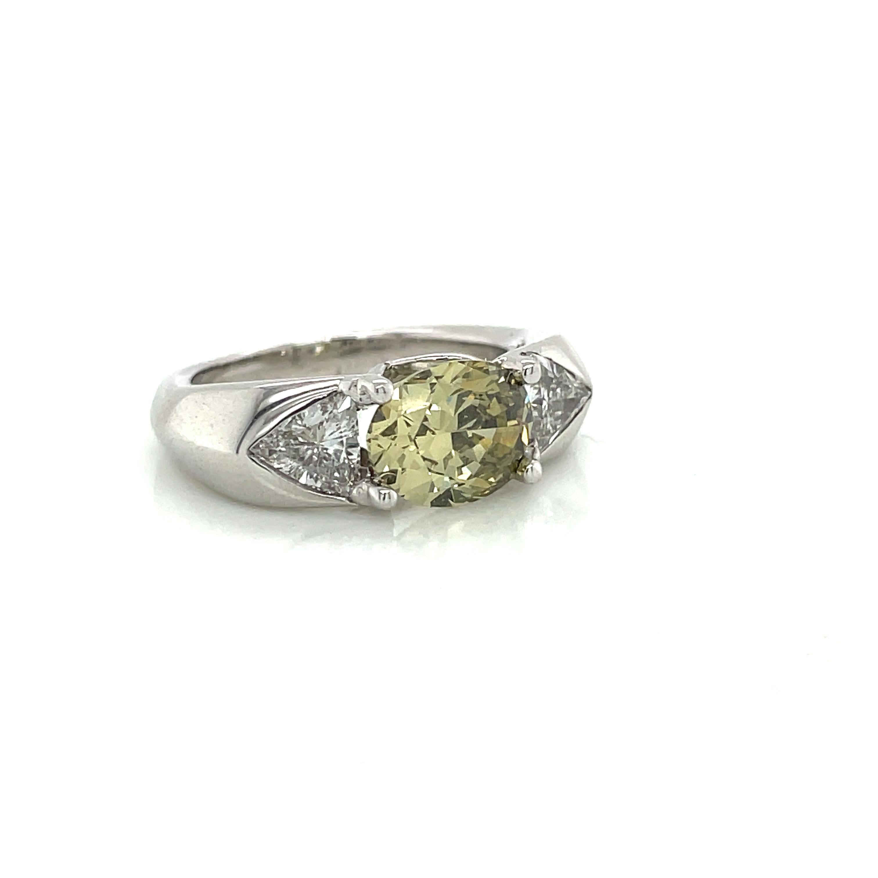 Wir lieben einen klobigen Rahmen und dieses supercoole Stück enttäuscht uns nicht. Ein ovaler Brillant von 1,80 Karat Fancy-Farbe ist in Ost-West-Richtung zwischen zwei erstaunlichen eisigen Billionen gefasst. Die Farbe ist so einzigartig - ein