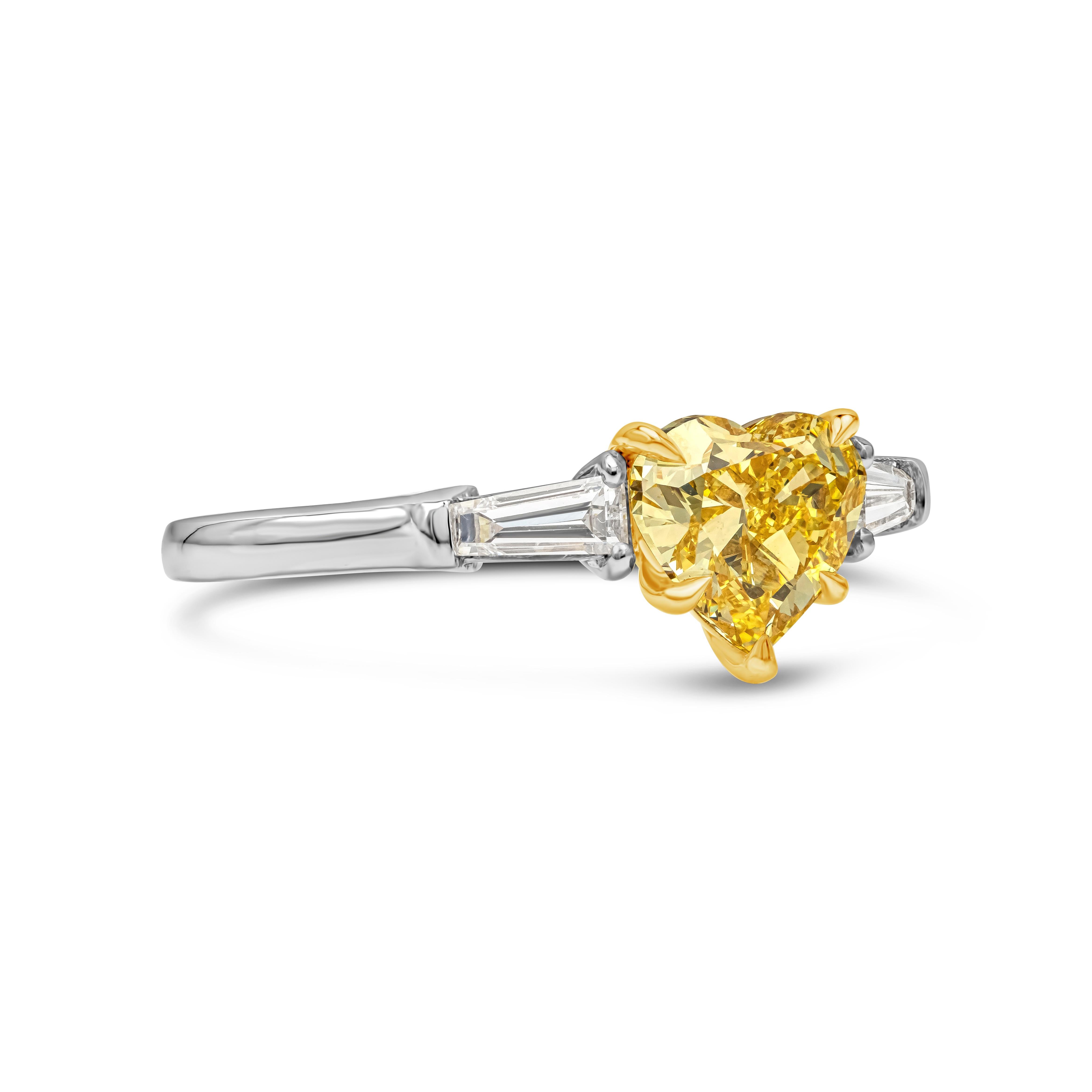 A unique and color-rich three-stone engagement ring design showcasing a 1.01 carats heart shape yellow diamond certified by GIA as Fancy Vivid Yellow color, VS2 in clarity, flanked by tapered baguette diamonds on each side. Accent diamonds weigh