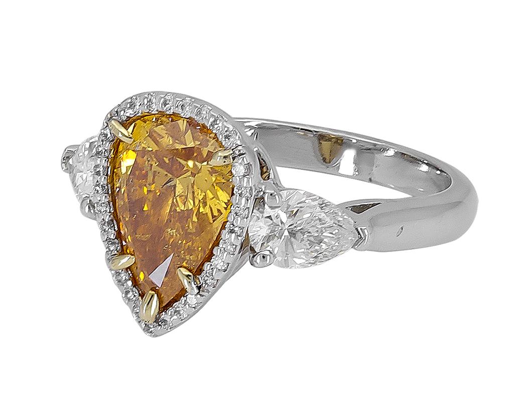 Features a color-rich pear shape diamond, surrounded by a row of round brilliant diamonds. Finished with pear shape diamonds on either side in a platinum mounting. 
GIA certified the center diamond as 2.20 carats, Fancy Vivid Yellow Orange