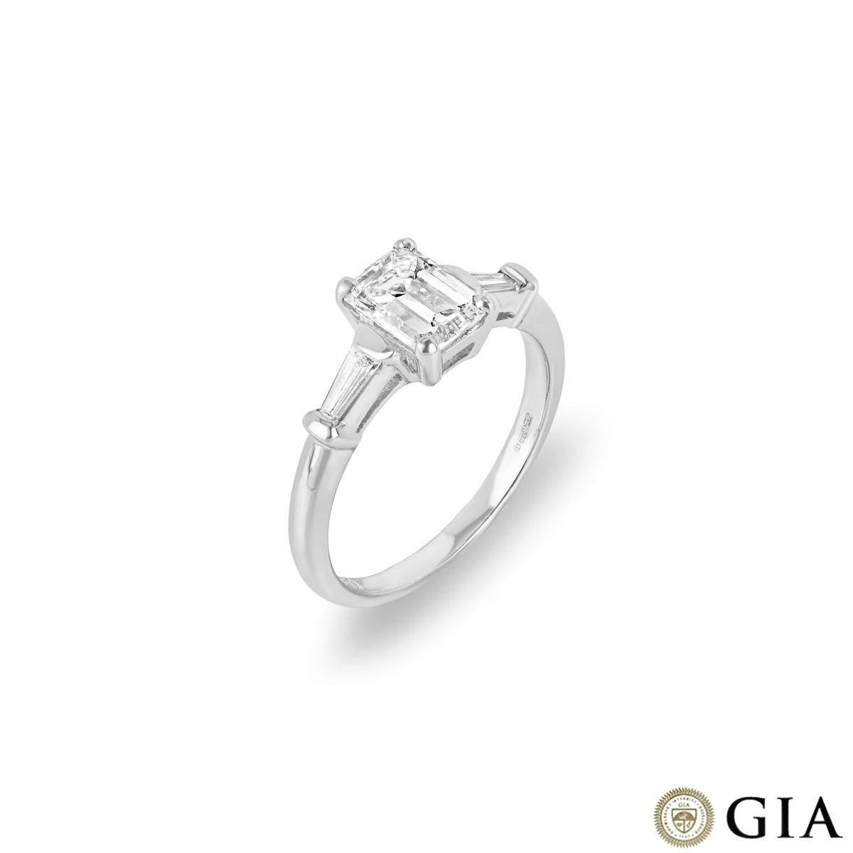A modern 18k white gold diamond three-stone ring. The engagement ring is set to the centre with an emerald cut diamond weighing 1.00ct, F colour and VS1 clarity. Accentuating the centre diamond are 2 tapered baguettes tension set to the shoulders