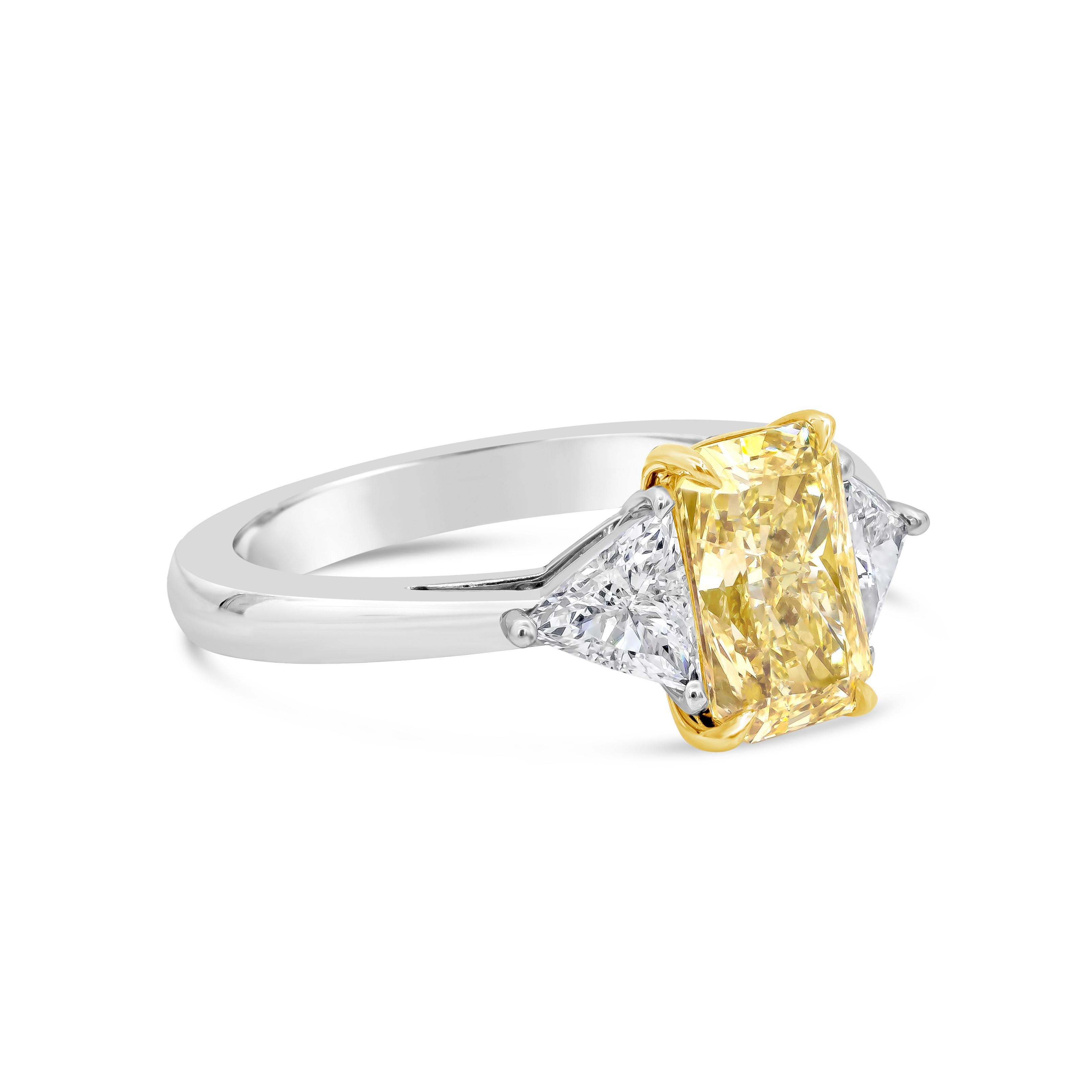 A gorgeous three-stone engagement ring, featuring a 2.02 carats radiant cut diamond certified by GIA as Fancy Yellow color and I1 clarity, set on a four claw prong basket made of 18K yellow gold. Flanked by trillion cut diamonds weighing 0.59 carat