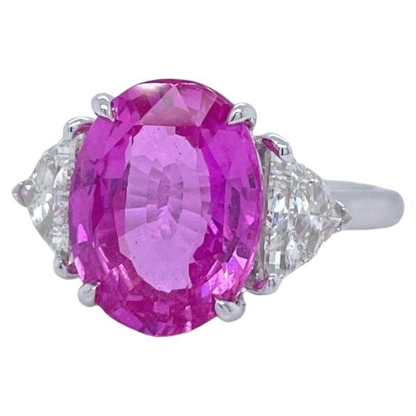 Der Ring enthält einen GIA-zertifizierten 12x9 mm großen ovalen rosa Saphir (5,18ct) und zwei seitliche Diamanten im Brillantschliff (0,79tcw). Der rosa Saphir und die Diamanten sind in einer handgefertigten Zackenfassung mit einem 2 mm breiten
