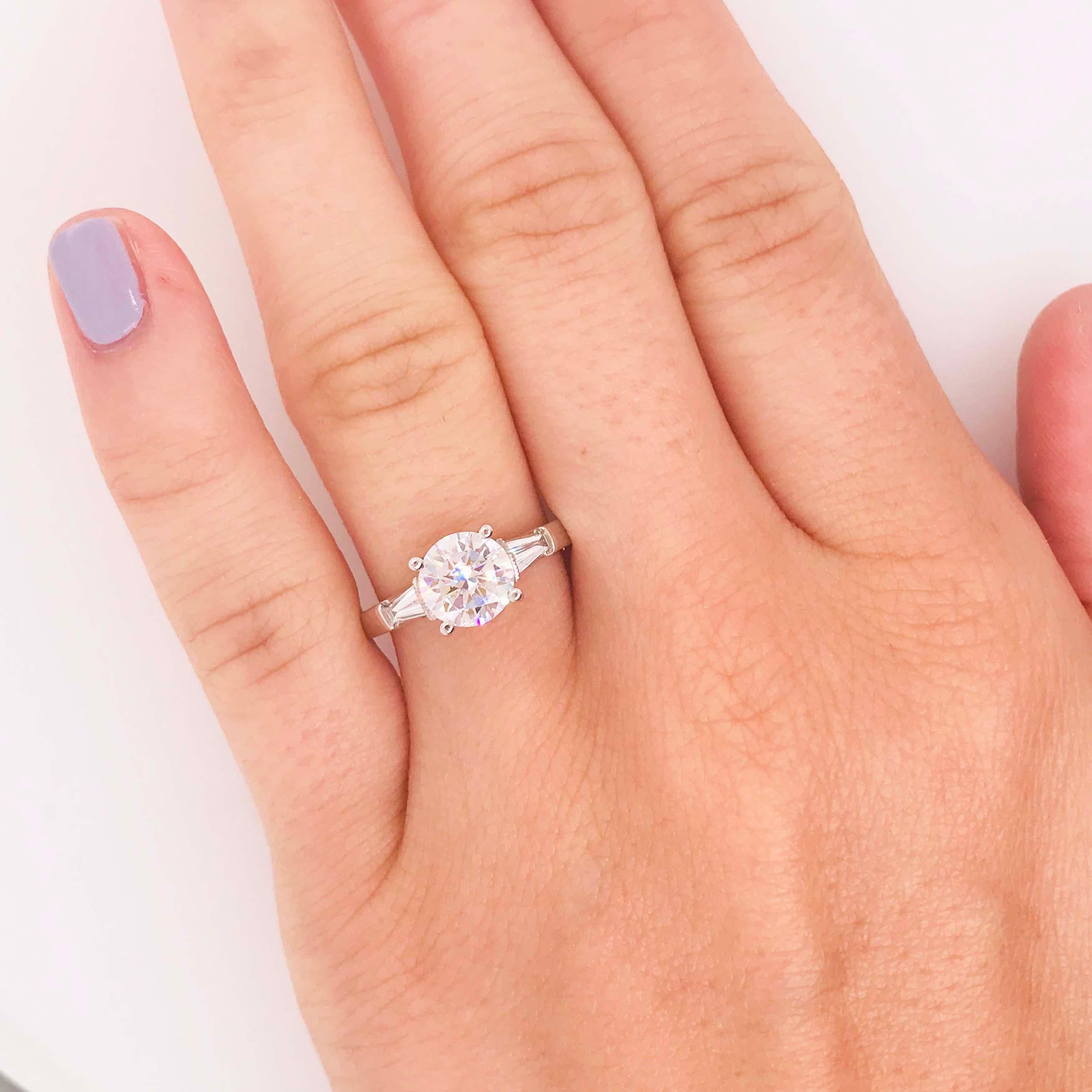 The stunning traditional three stone diamond engagement ring is a classic design! With a GIA certified round brilliant diamond set in the center. The center diamond is flanked by a tapered baguette on each side. This ring has a total diamond carat