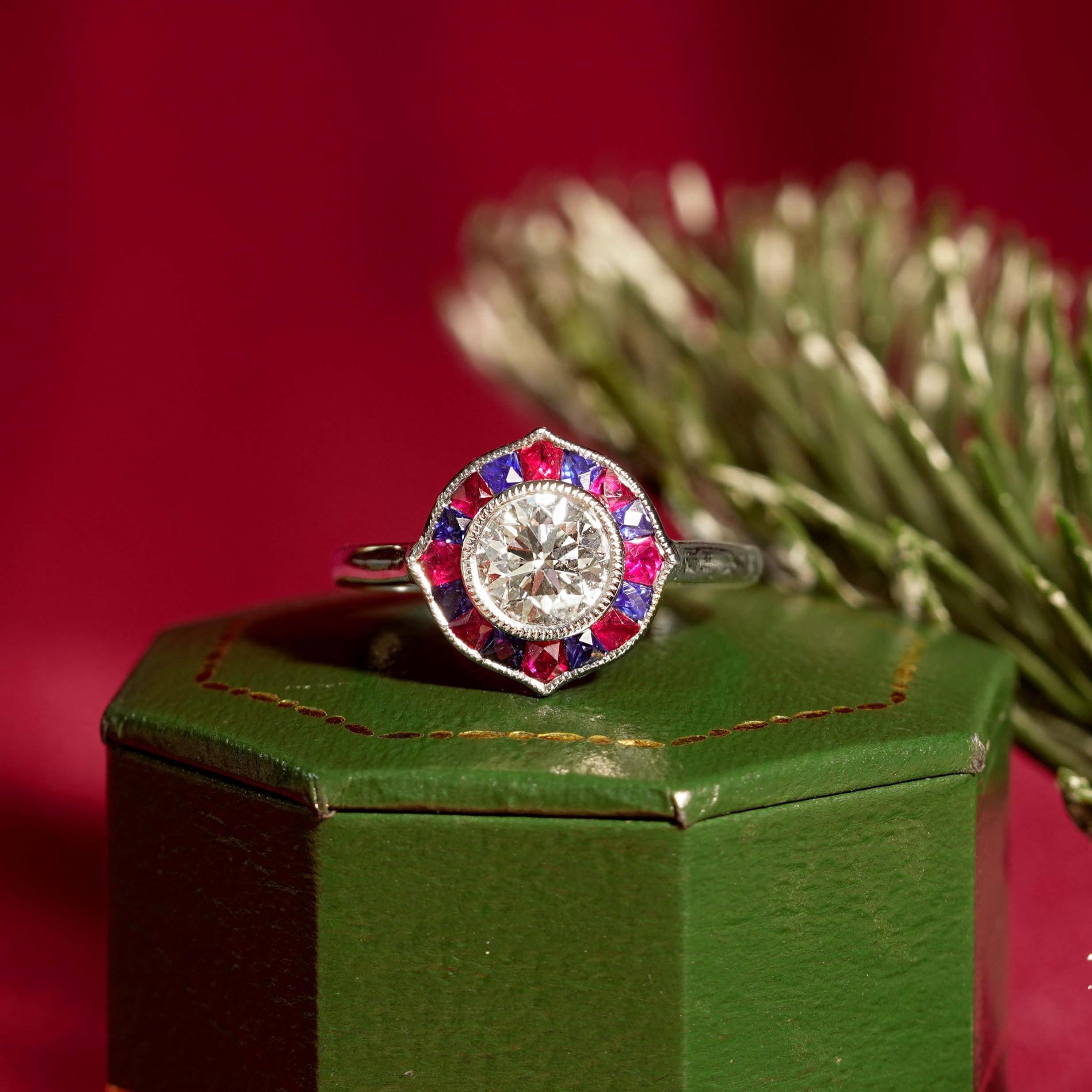 Dieser atemberaubende Halo-Ring funkelt in glänzendem Platin 950 und verfügt über einen runden Diamanten von 1 Karat in der Mitte mit einem Rubin und einem Saphir im französischen Schliff in einem wunderschönen Halo-Design. Schmücken Sie sich mit