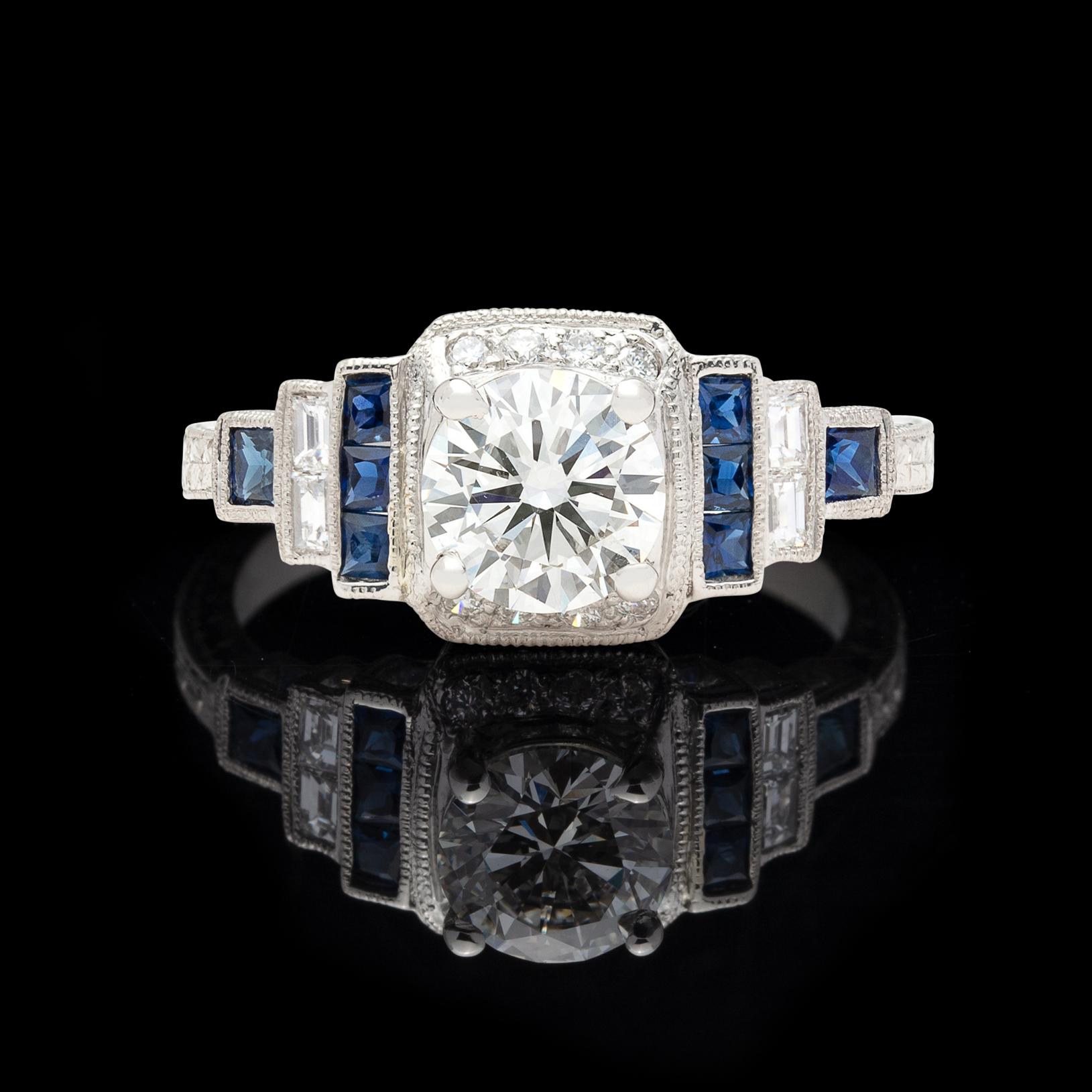 Inspired by Art Deco stylings, the tapering platinum engagement ring features a GIA  J color and SI1 clarity 1.00 carat round brilliant-cut diamond, with stepped shoulders set with 12 round brilliant and baguette-cut diamonds, as well as 8