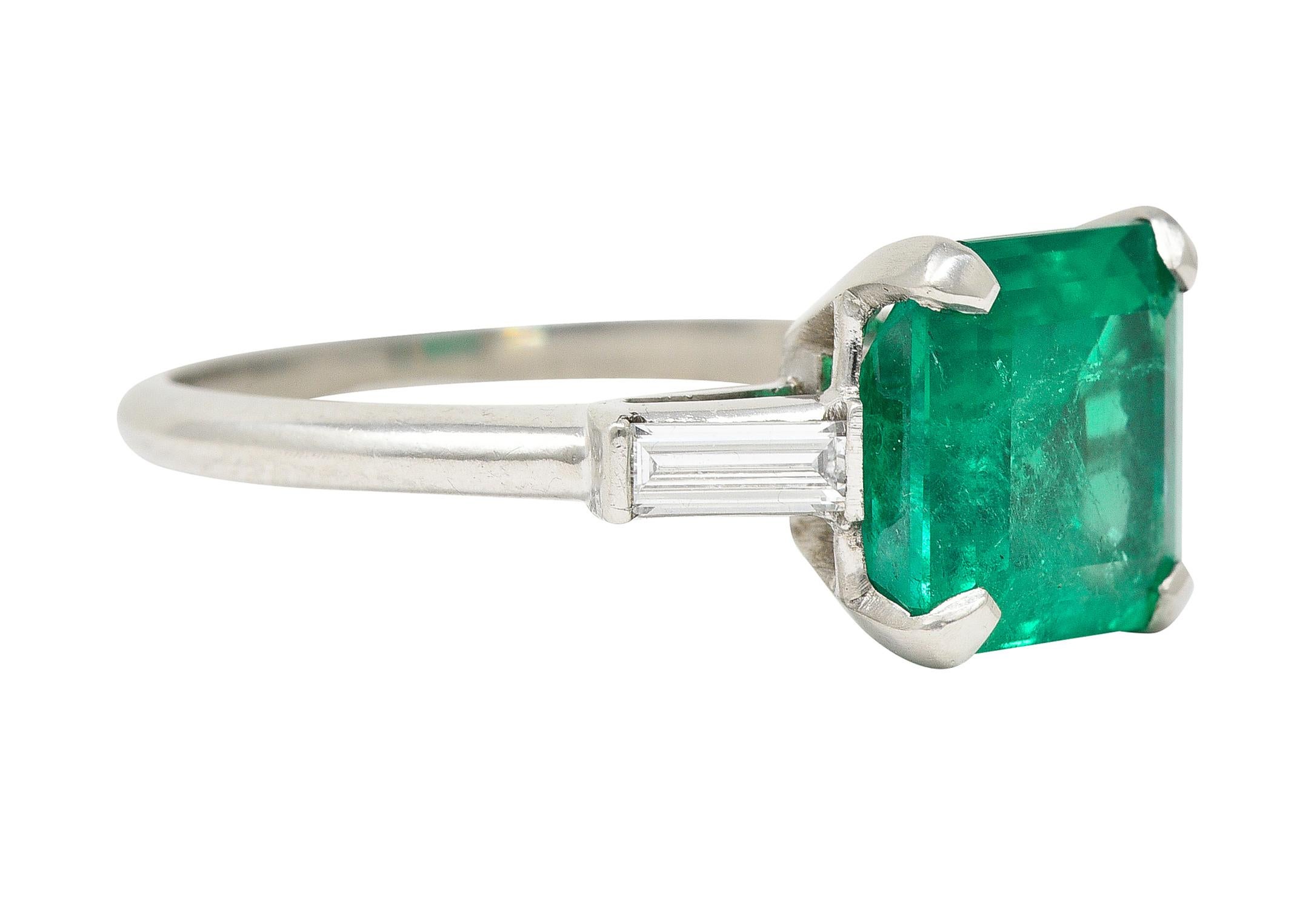 Centering a square step-cut emerald weighing 3.24 carats - transparent medium green. Natural Colombian in origin with F1 clarity enhancements - prong set in basket. Flanked by baguette cut diamonds bar set East to West. Weighing approximately 0.24