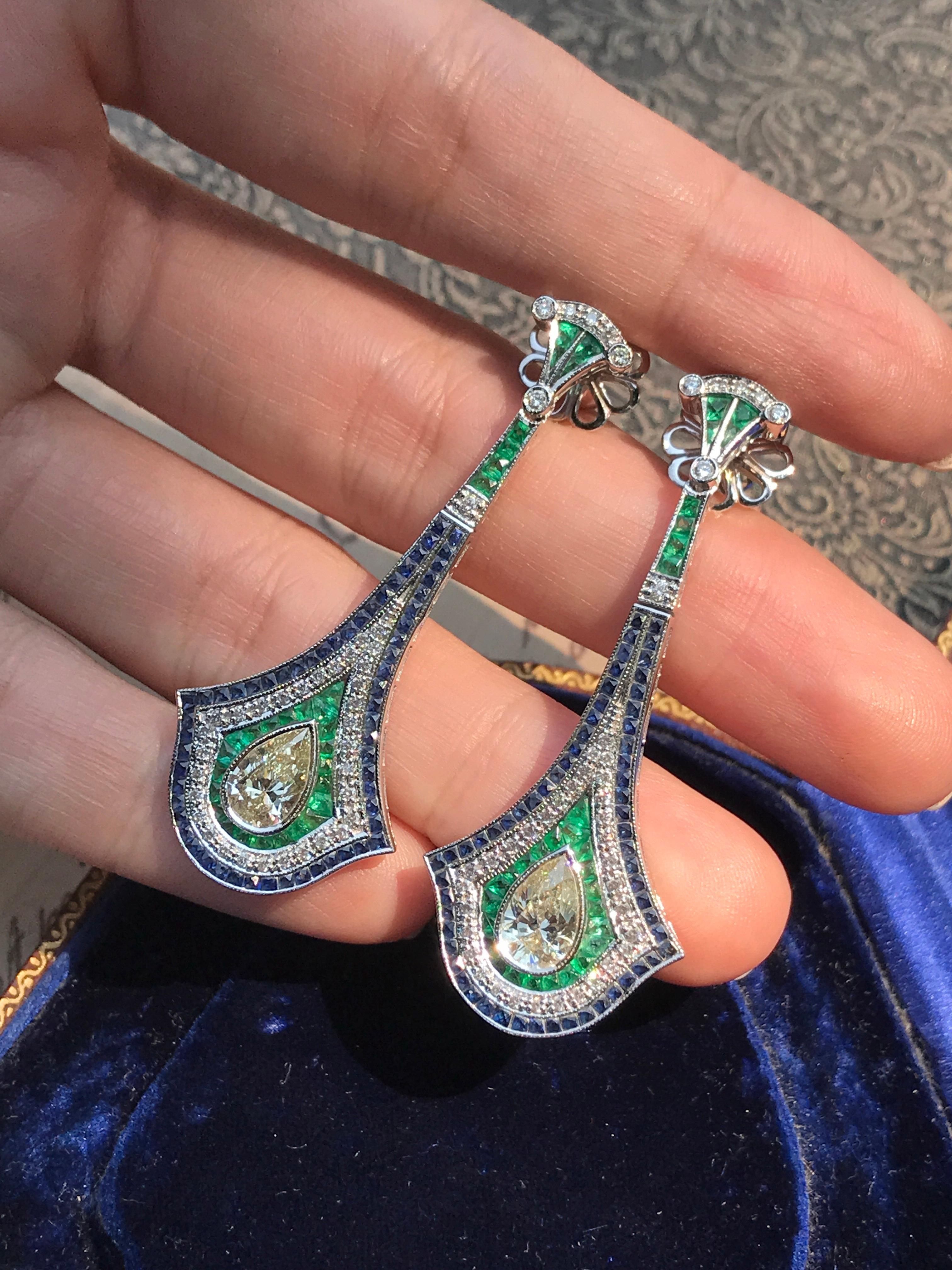 Extraordinary GIA certified pear shape diamond with emerald and sapphire Art Deco inspired earrings, all mounted in 18K white gold. The inner-halo is set with French cut vivid green emeralds. The outer-halo set with white round brilliant diamond and
