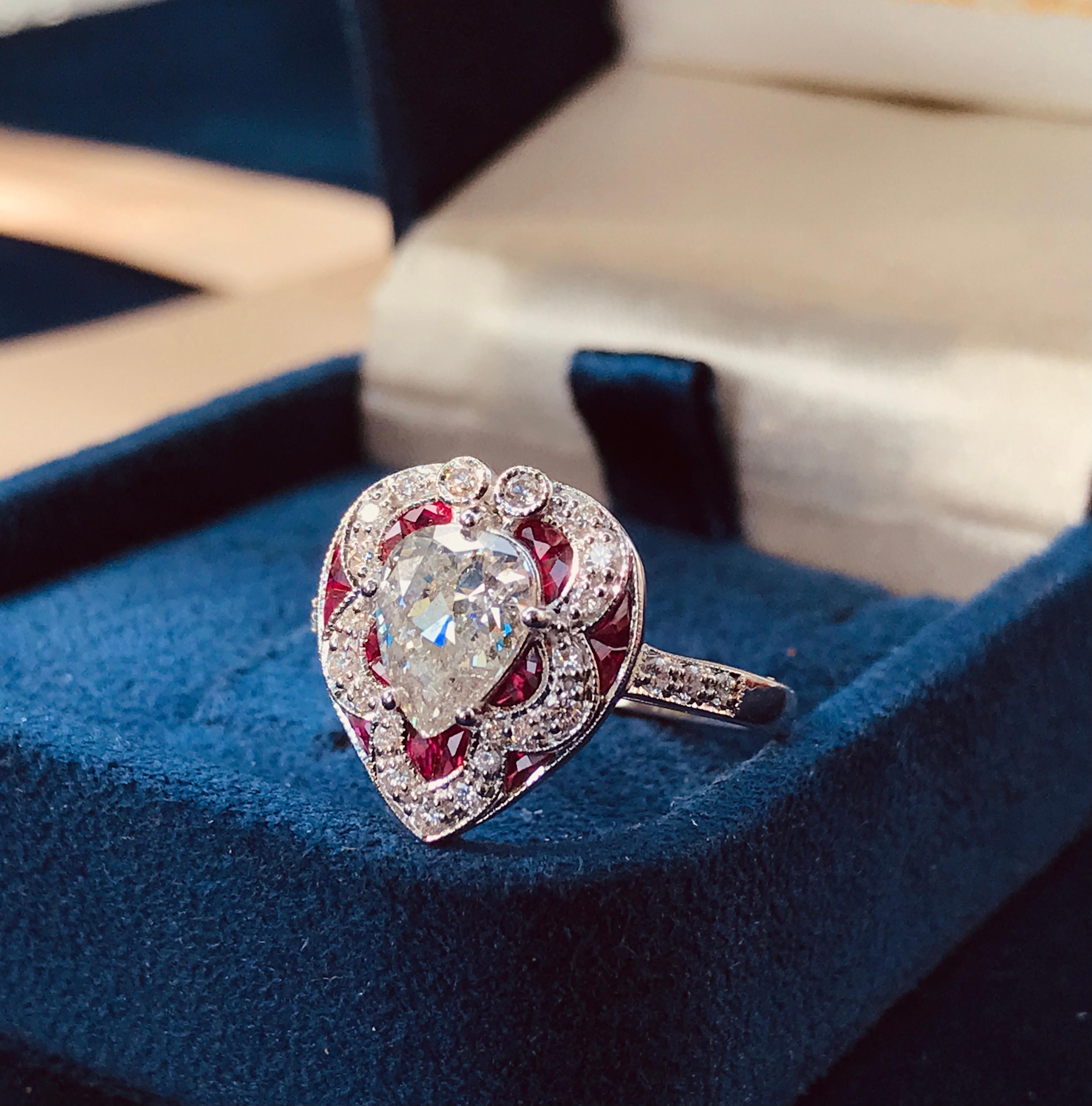 Im Mittelpunkt steht ein funkelnder birnenförmiger Diamant von 1,05 ct. (Farbe I, Reinheit I1), umrahmt von Rubinen im französischen Schliff und zusätzlich besetzt mit siebenundzwanzig runden Diamanten von ca. 0,23 Karat Gewicht, gefertigt in 18