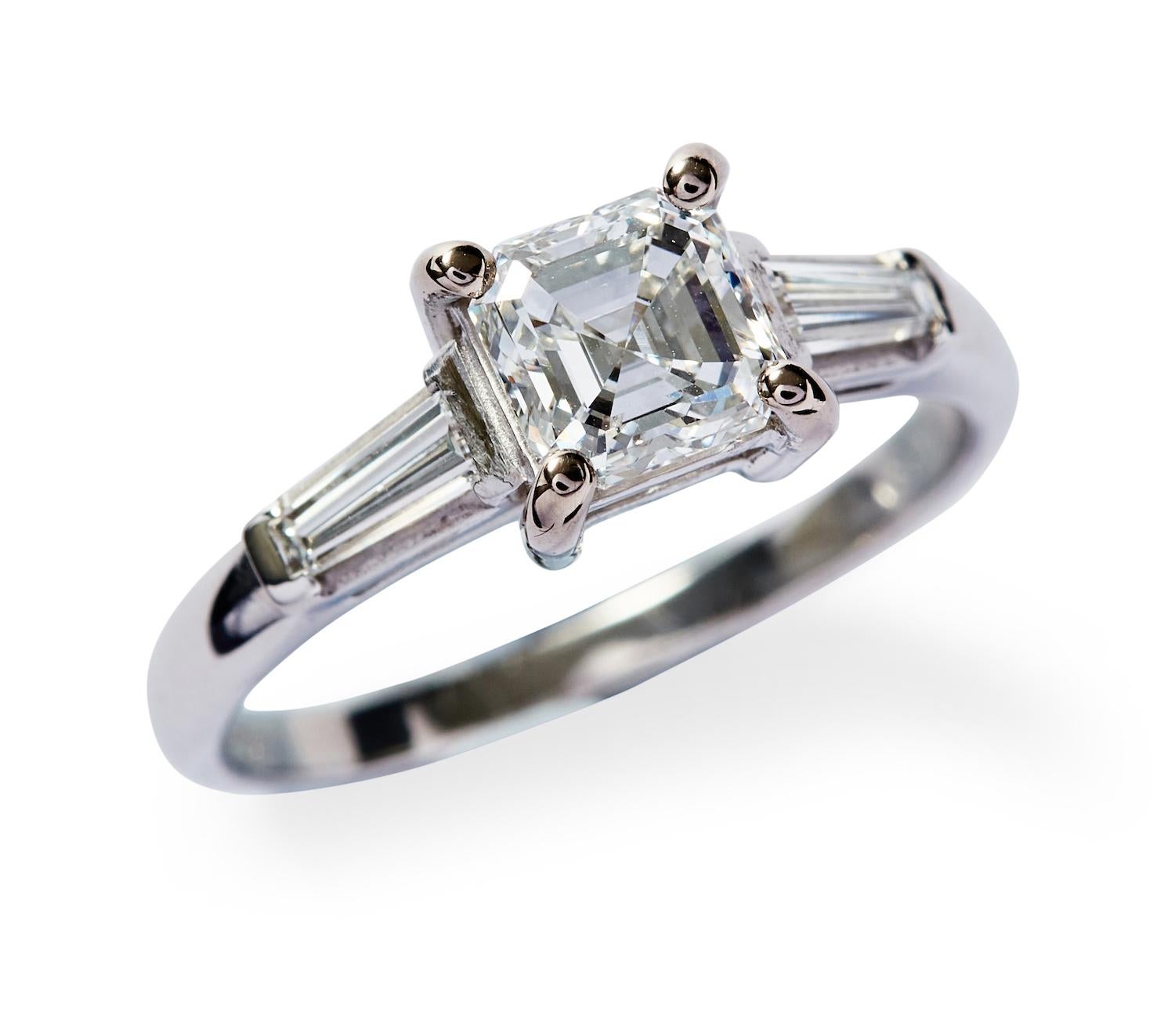 Unique features: 
SOLITAIRE DIAMOND RING 
The emerald-cut diamond weighing 1.02 carats, is claw-set between a pair of tapered baguette diamonds, mounted in 18ct white gold, size M. 

Accompanied by a GSL report numbered AA53882

Metal: 18ct White