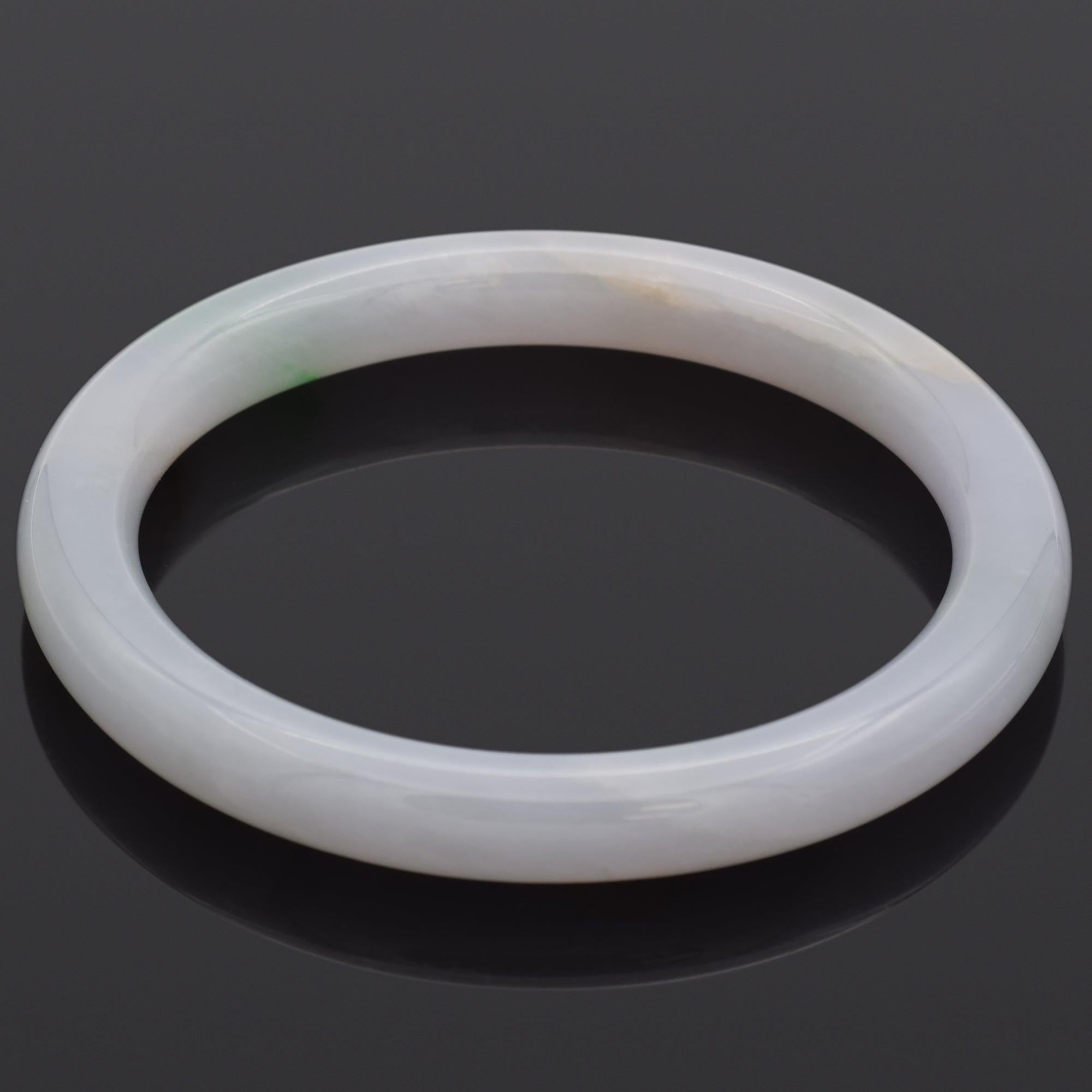 This bangle bracelet is carved from natural jadeite jade, a rare and valuable form of jade known for its density, translucency, and vibrant colors. The bracelet features variegated hues — primarily purple-gray and natural green — which blend