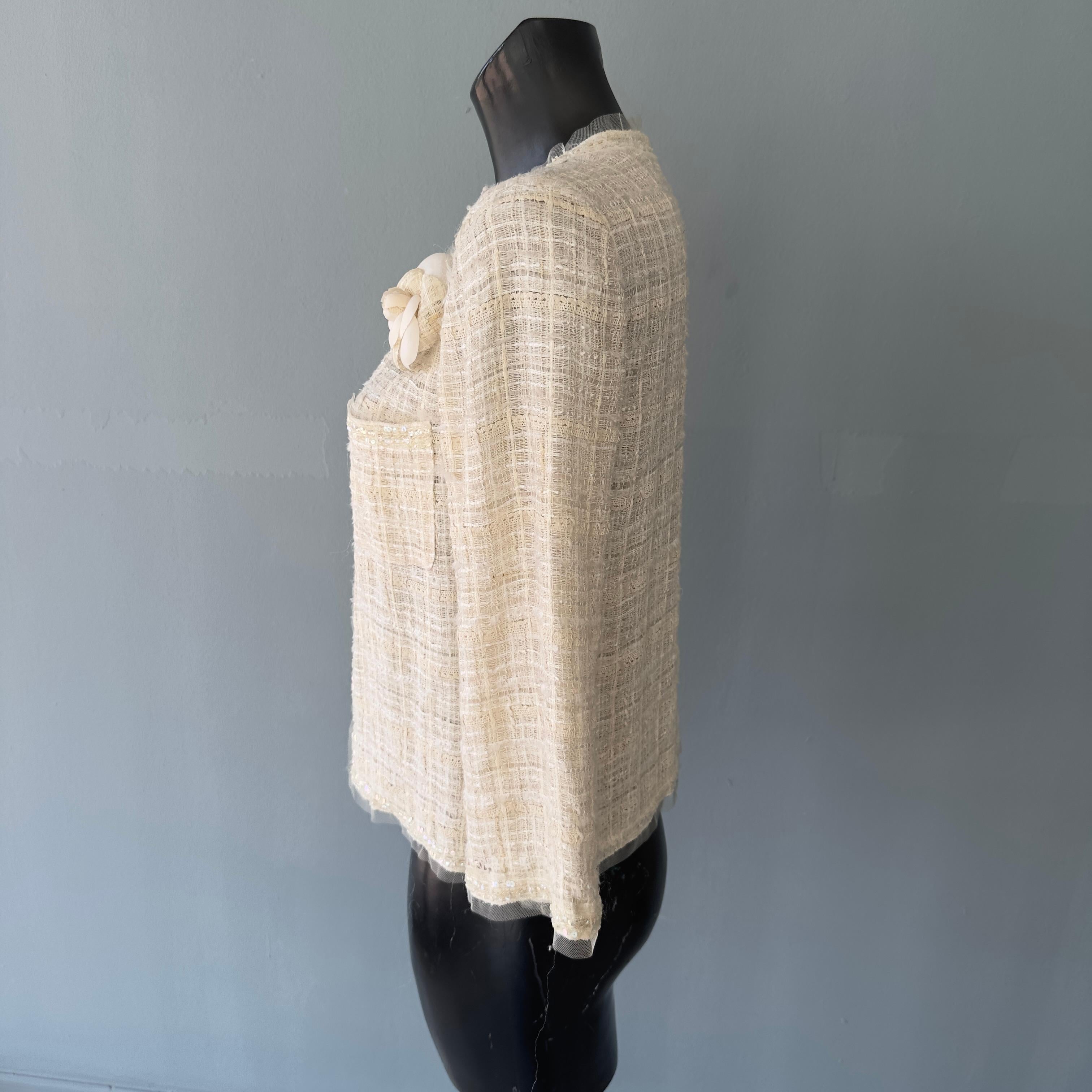 Cotton Chanel jacket with woven work, voile on edges and pockets embellished with sequins all tone on tone. To complete the brooch with the same colors and fabrics in the shape of the classic camellia that represents the brand 
Its very light cream
