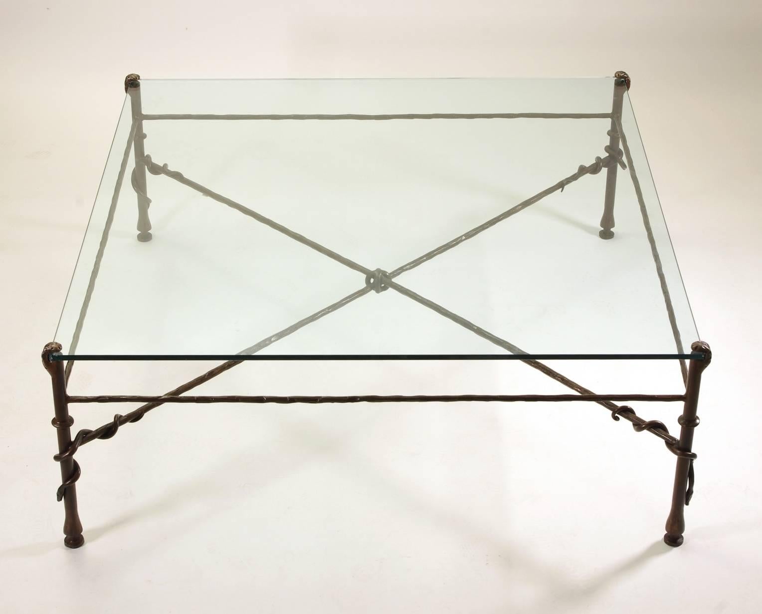 Giacometti inspired wrought iron and glass coffee table, the glass plate supported by four legs, each with an entwined snake, joined by an X-stretcher tied with a knot.