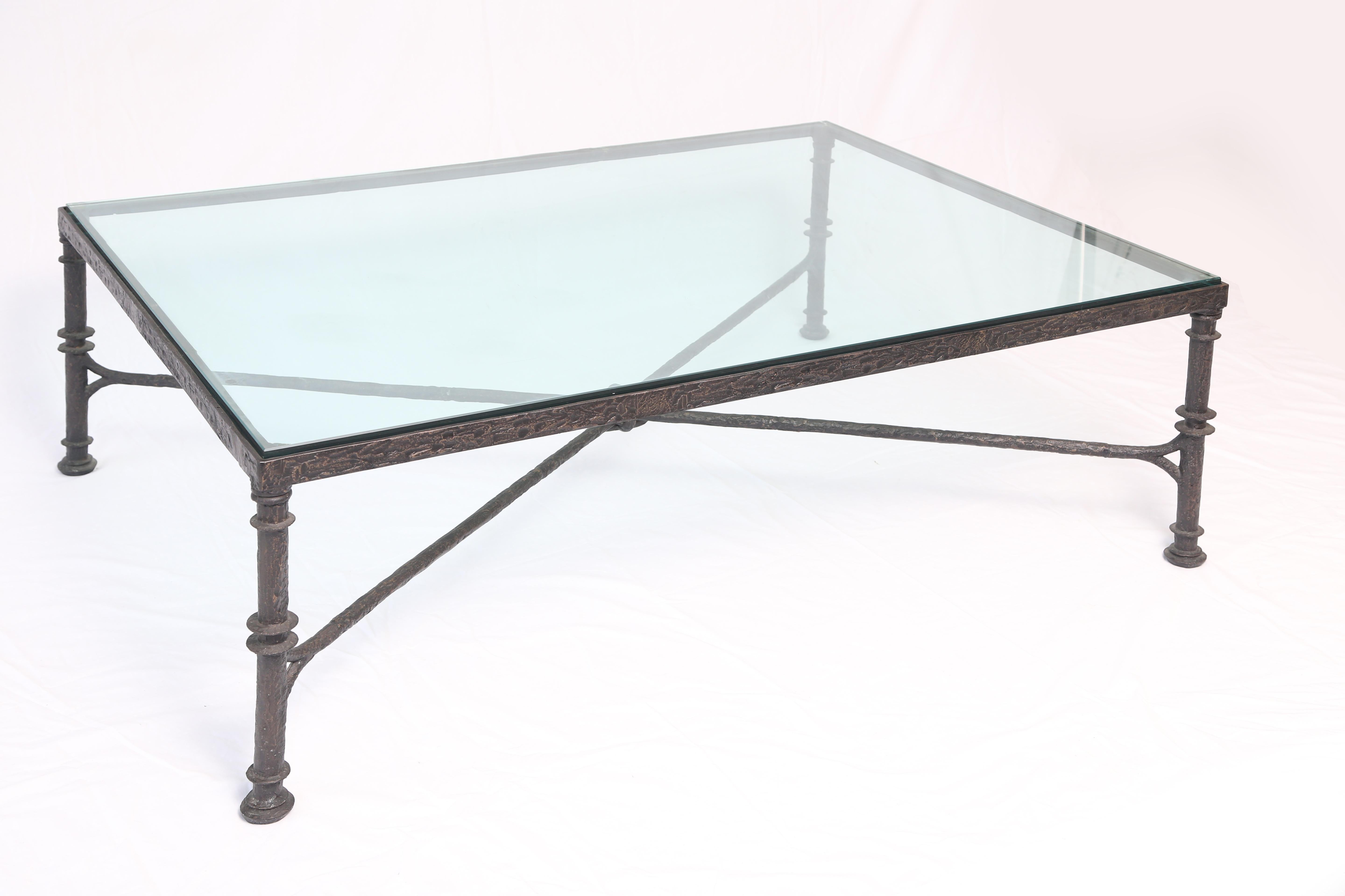 The rectangular glass top set within a conforming bronze base raised on round legs joined by an X-form stretcher with knot-details.