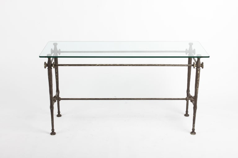 In the style of artist Diego Giacometti, this hammered and sculpted metal glass top console table has applied bronze paint over an under coat of yellow and green. Applied wear to finish, scratches to glass top.