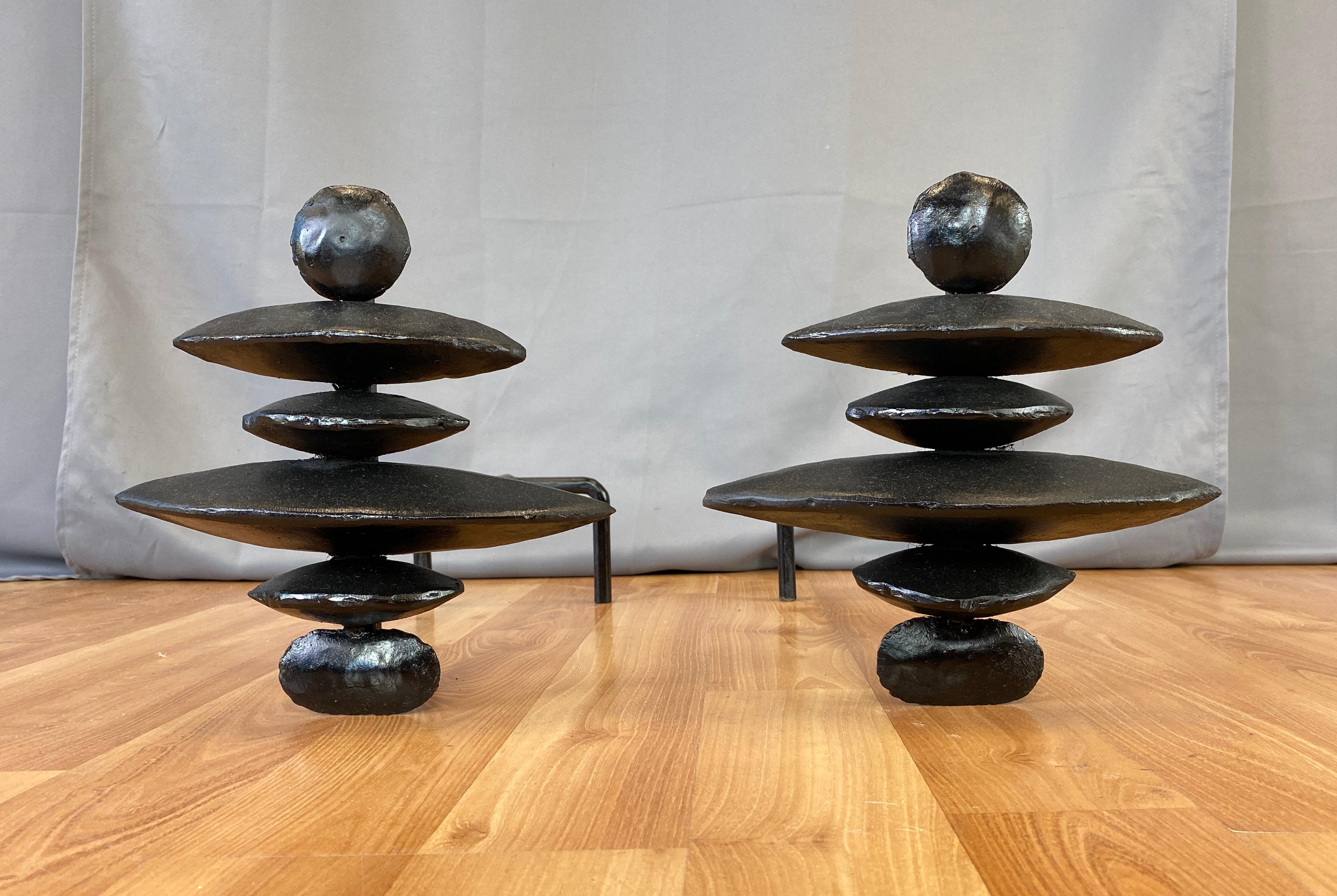 A Brutalist pair of andirons in the style of Alberto Giacometti's.
Total of twelve black looking rocks stacked one on top of the other, like cairns in the wilderness.
Metal rod coming out from their back side, that then form two legs.