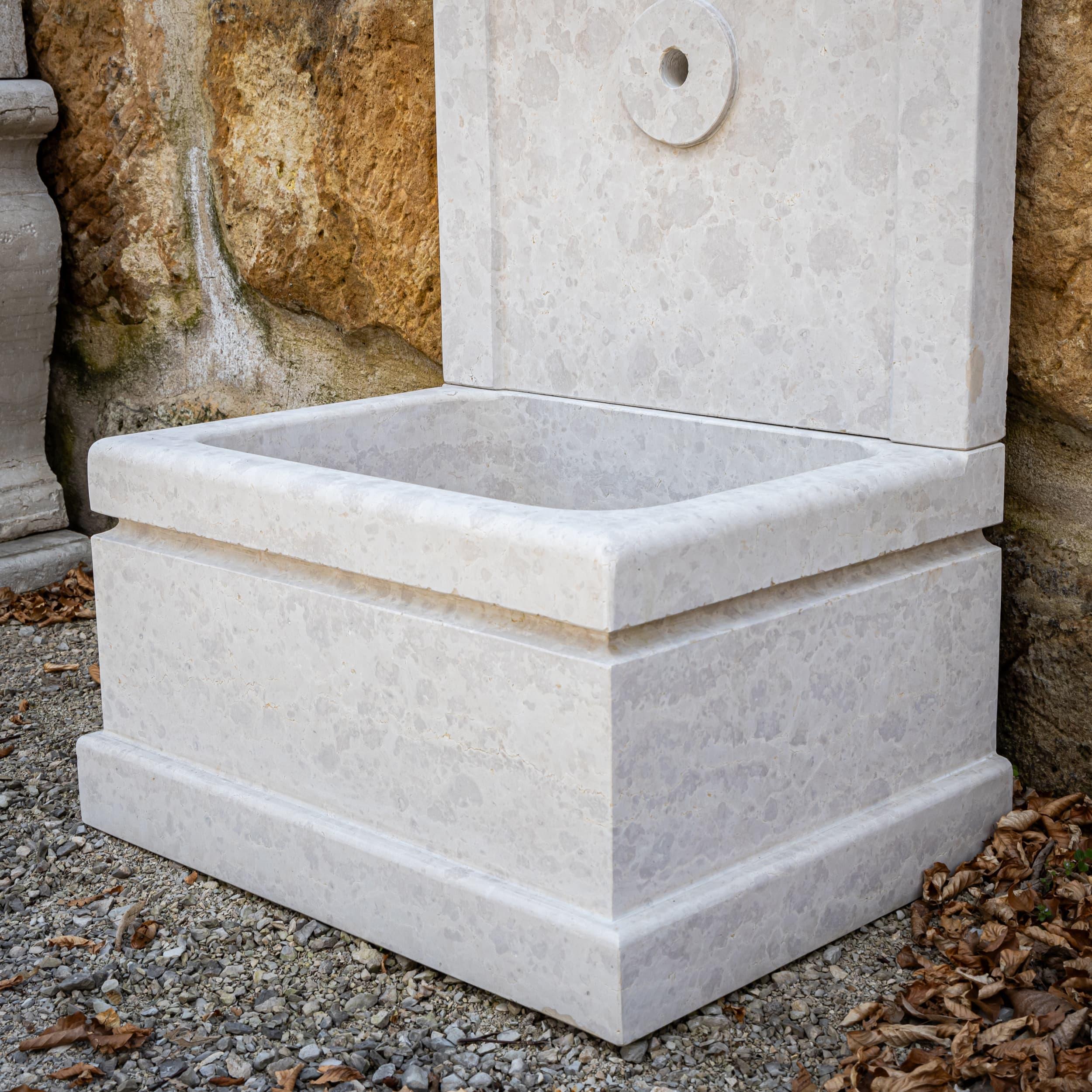 Fuente mural de piedra natural Giallo d'Istria con pila rectangular y trasera curvada. Las finas volutas y el detalle de la roseta central dan al sencillo diseño un toque clásico y una gran estabilidad.
