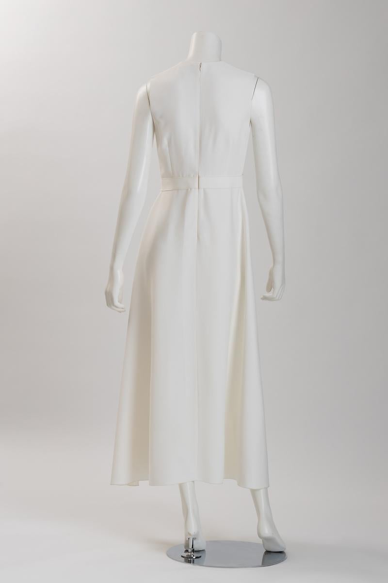 L'élégante robe de mariée sans manches en crêpe ivoire de Giambattista Valli présente un délicat buste ajusté, des pinces pour accentuer la longueur de la taille, qui se termine par un ruban cousu à la ceinture. Une fermeture à glissière cachée