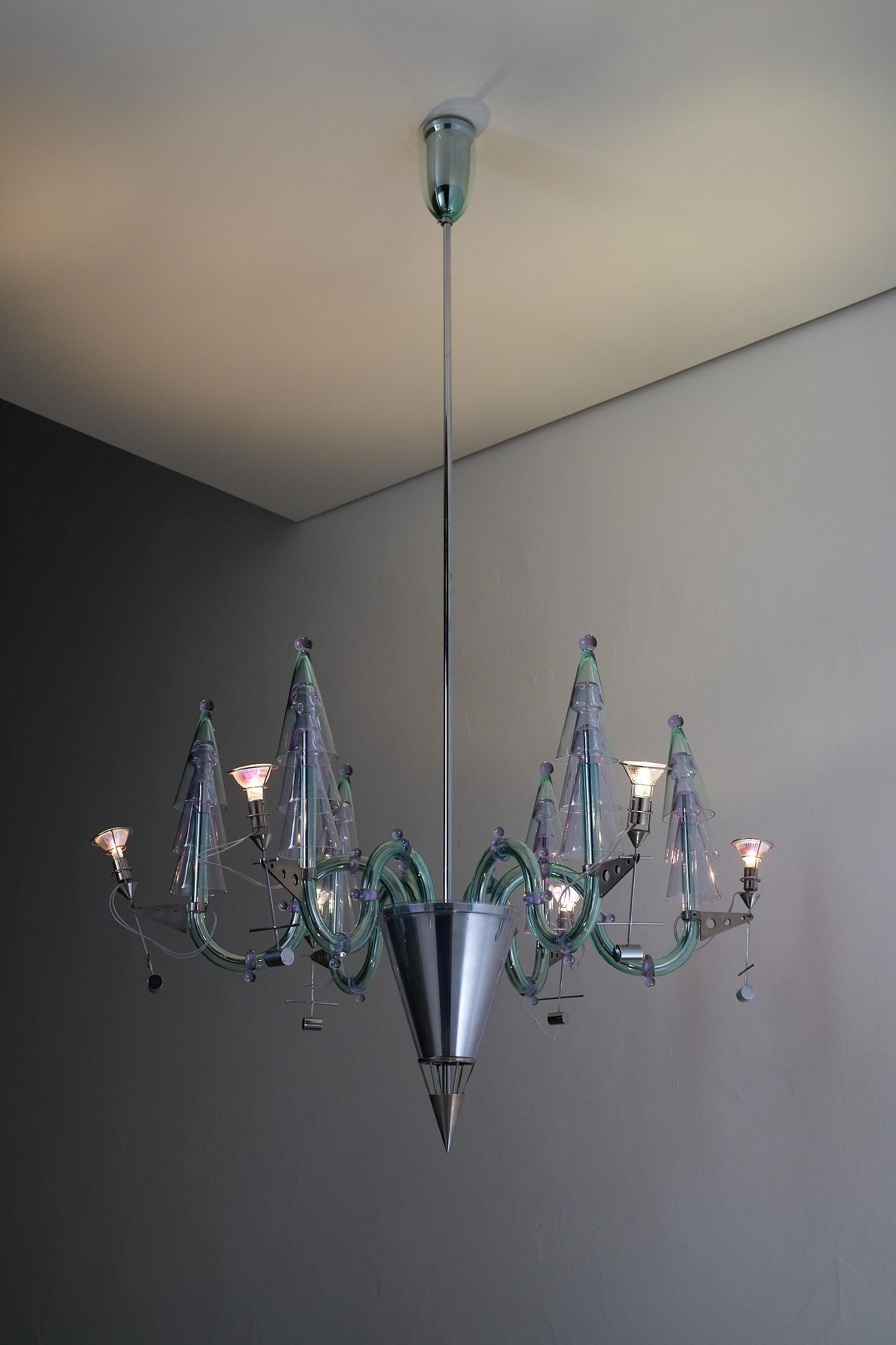 Lampadario in vetro di Murano di Gian Paolo Canova e Carlo Moretti. Questo lampadario unico nel suo genere è dotato di 6 bracci e reca il marchio di Carlo Moretti sul vetro. La struttura è realizzata in acciaio cromato, mentre il vetro di Murano