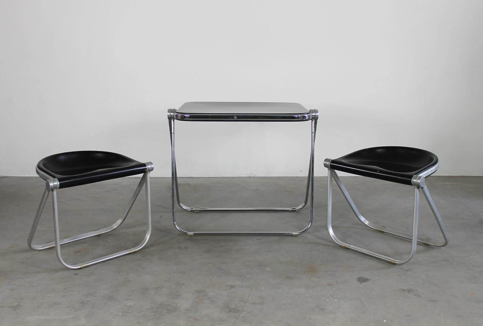 Set composed by one Platone folding table with structure in chromed steel and die-cast aluminum, table top in black polyurethane and a couple of Pluff folding stools with structure in tubular aluminum and die-cast aluminum, seat in black