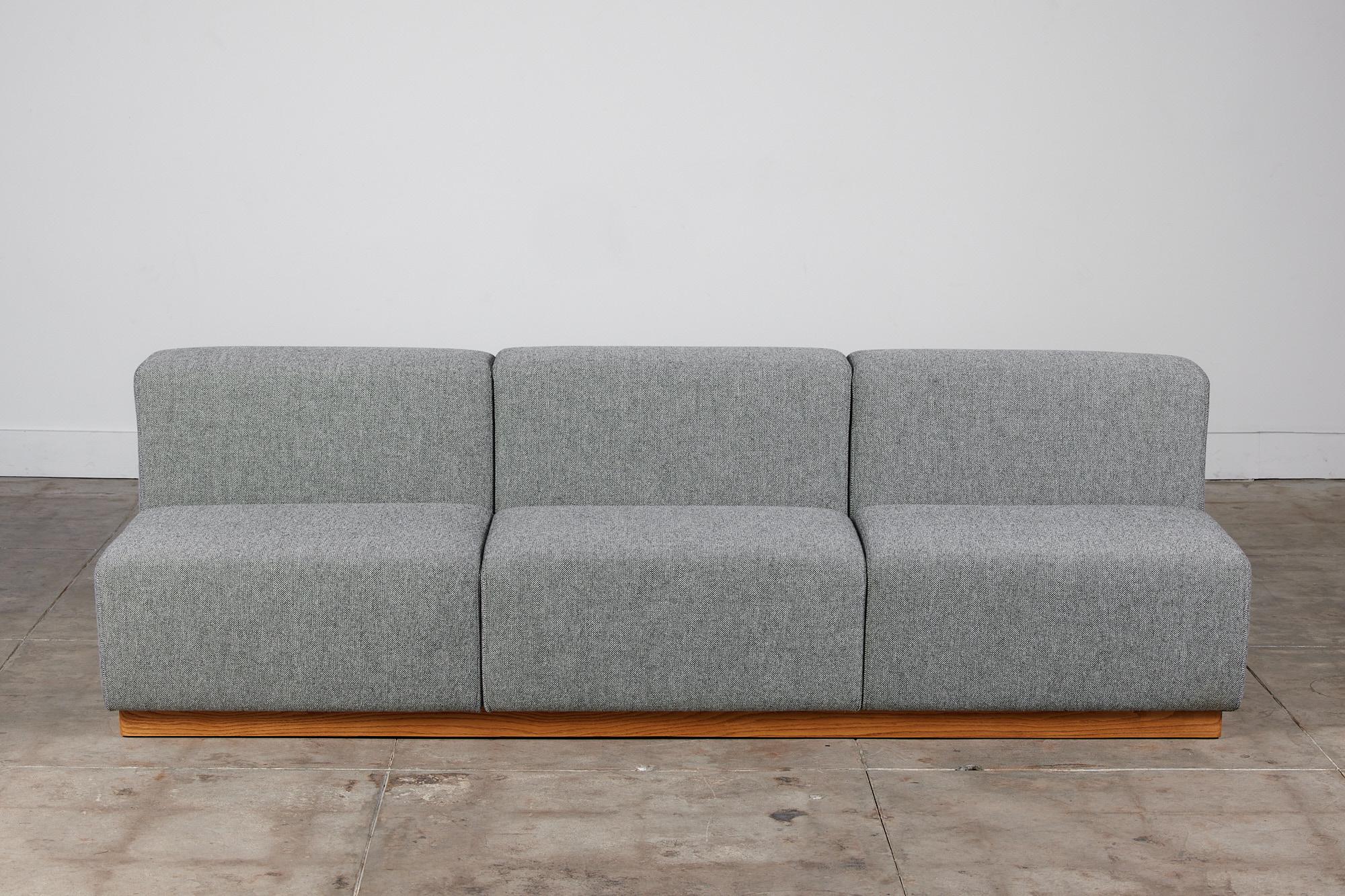 Modern cubic sofa in the style of Giancarlo Piretti. This sofa has been newly upholstered in Kvadrat fabric and features three seats with clean geometric lines. The sofa sits atop an oak plinth base. This semi modular sofa can be arranged with our