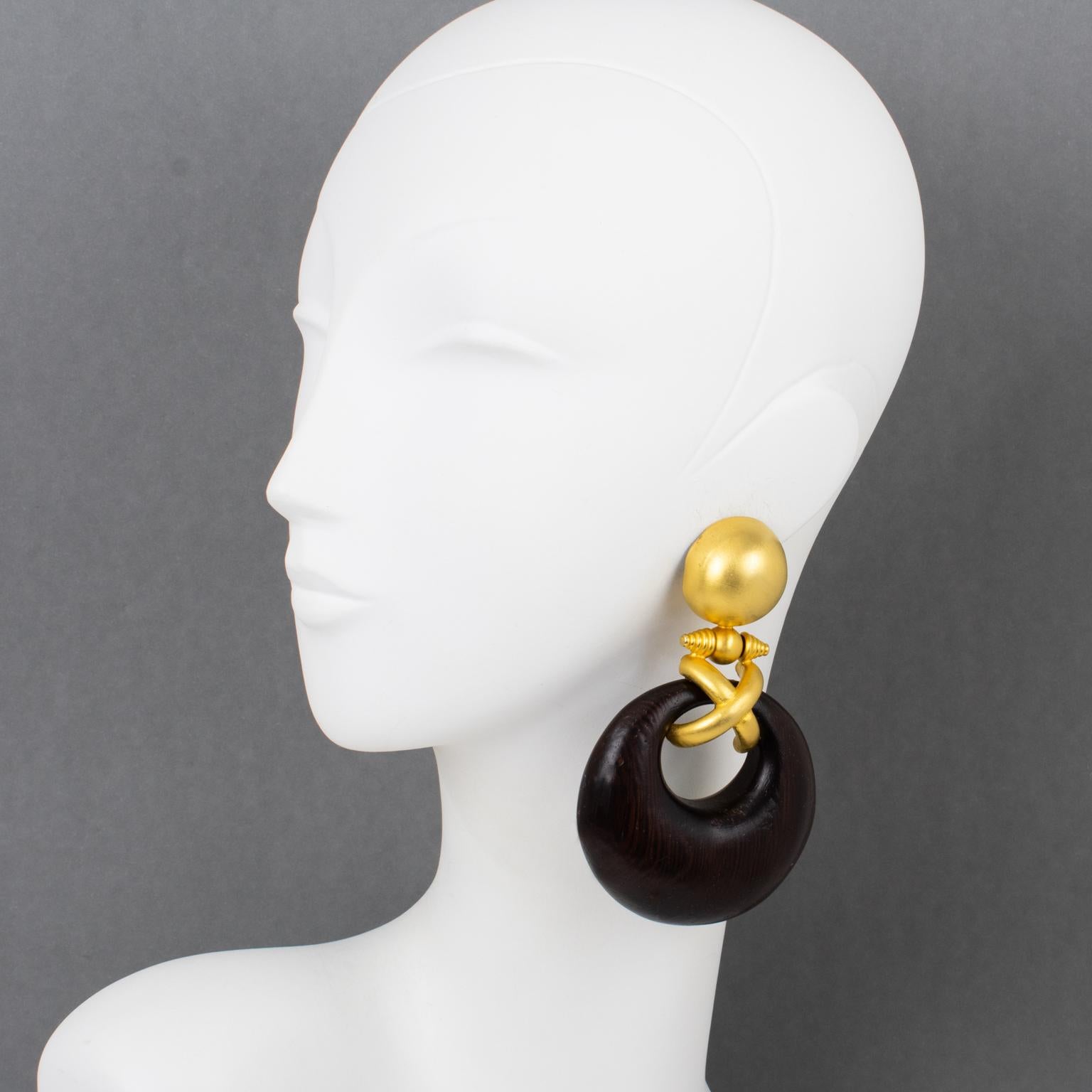 Italian designer Gianfranco Ferre created these spectacular couture clip-on earrings in the 1990s. The oversized shoulder duster design boasts a door-knocker shape with gilded metal in a semi-mat finish aspect, complimented with tropical wood