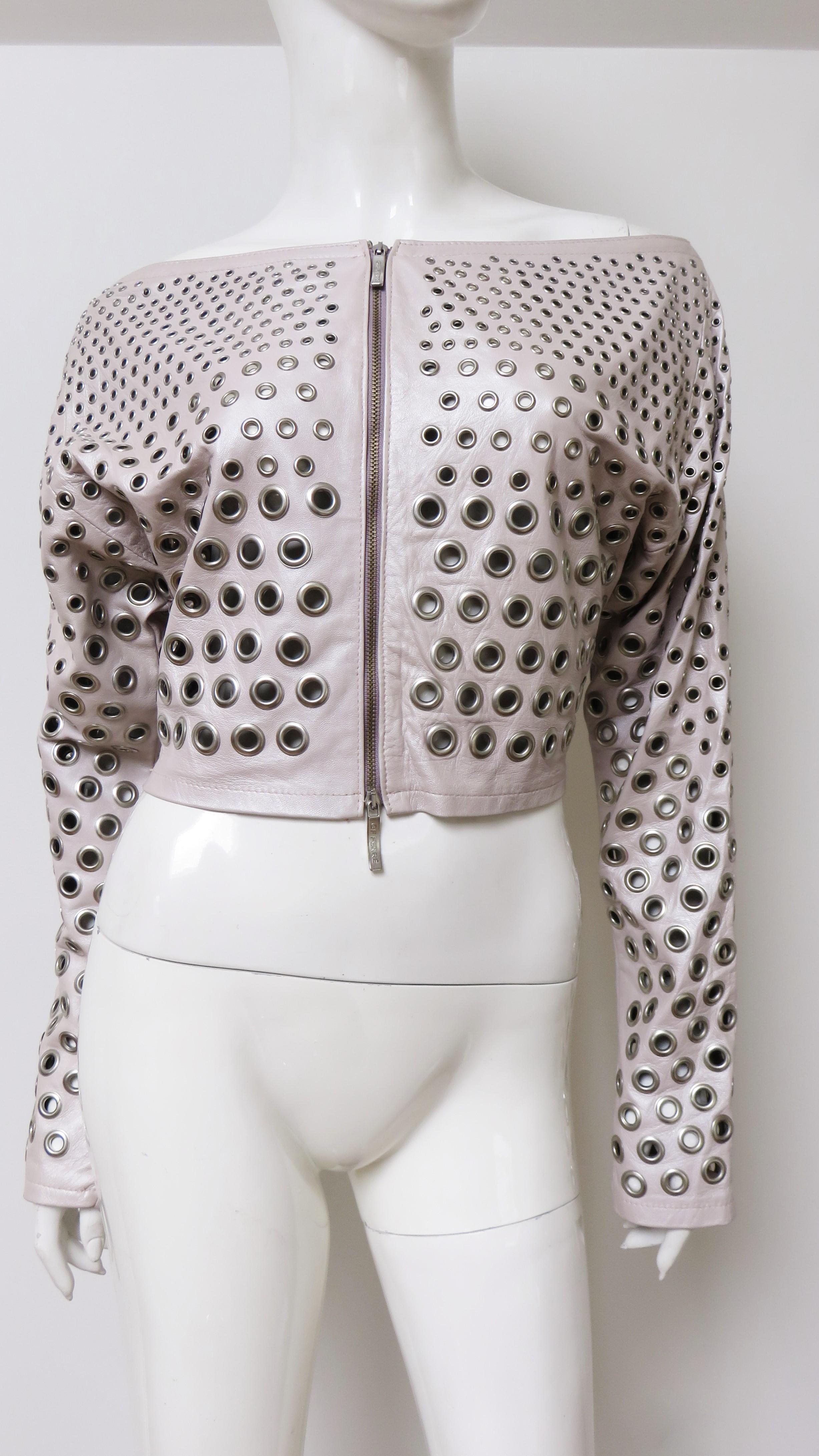 A fabulous shell pink leather crop jacket by Gianfranco Ferre.  It has a bateau neckline, long sleeves, and is covered in rows of silver gradating grommets smaller in size at the top of the jacket increasing in size towards the hem.  There is a