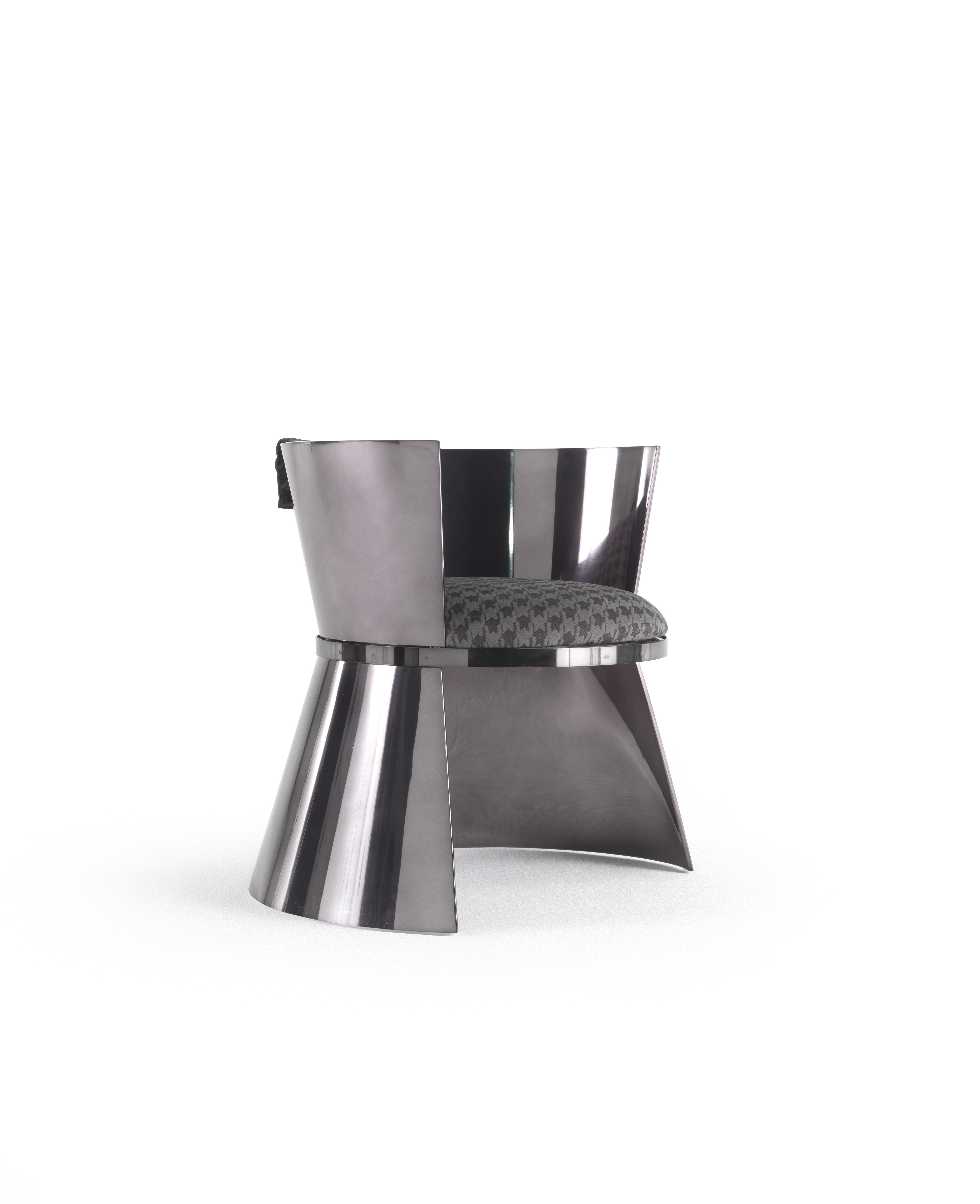 Un original sillón en forma de reloj de arena, caracterizado por la alternancia de componentes con acabado cromado gris humo londinense y brillante. La funda del asiento con tejido de pata de gallo añade una nota masculina a este mueble urbano y