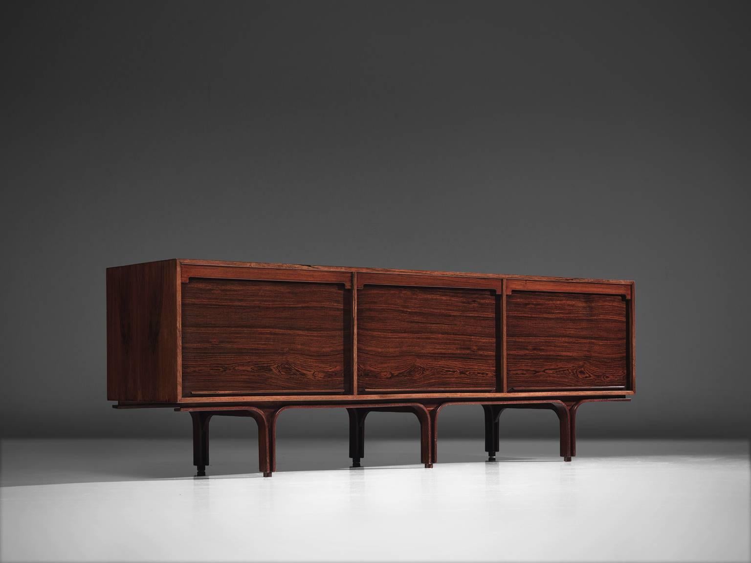 Gianfranco Frattini for Bernini, credenza, rosewood, Italy, 1960s.

This credenza in rosewood is designed by Frattini. It features the typical design traits of Frattini such as the tambour doors but also the legs that feature a border with