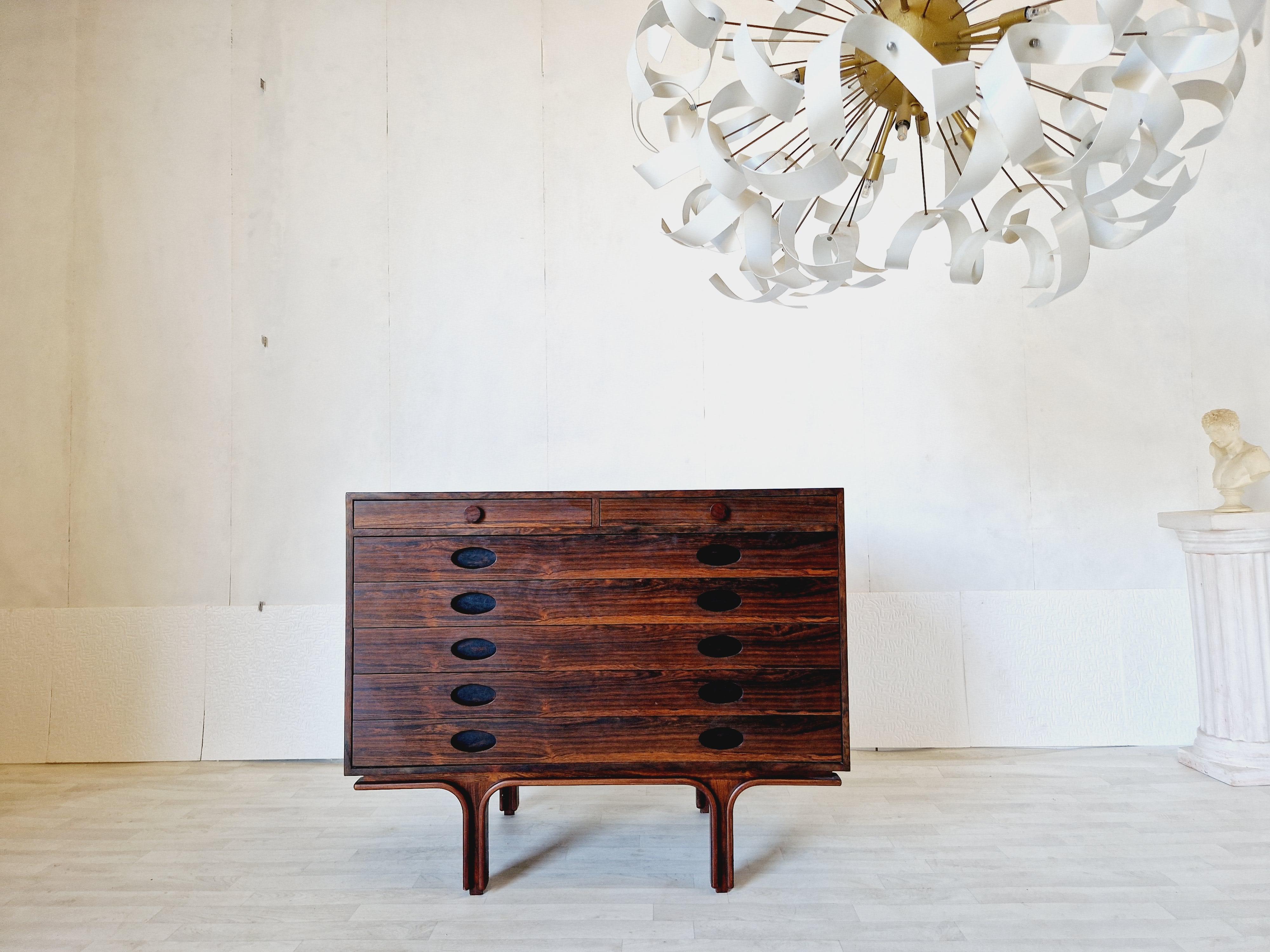 
This stunning vintage chest of drawers is a true statement piece for any room. It has a beautiful Rosewood finish and smooth features, with cup handles that add a touch of mid-century modern style. The seven original drawers provide plenty of